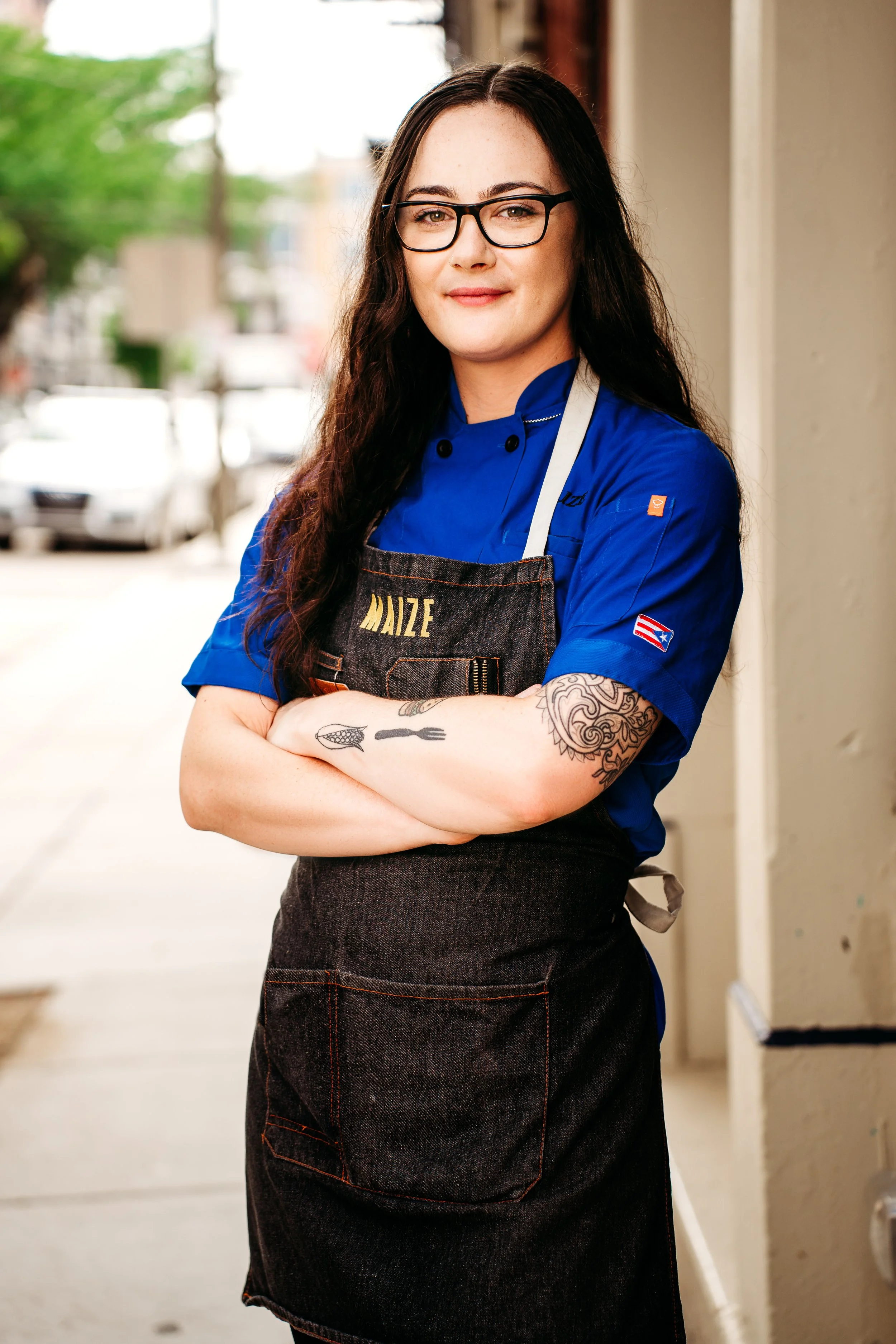 Photo of Chef Jessica Baston in chef coat and apron that says "Maize"