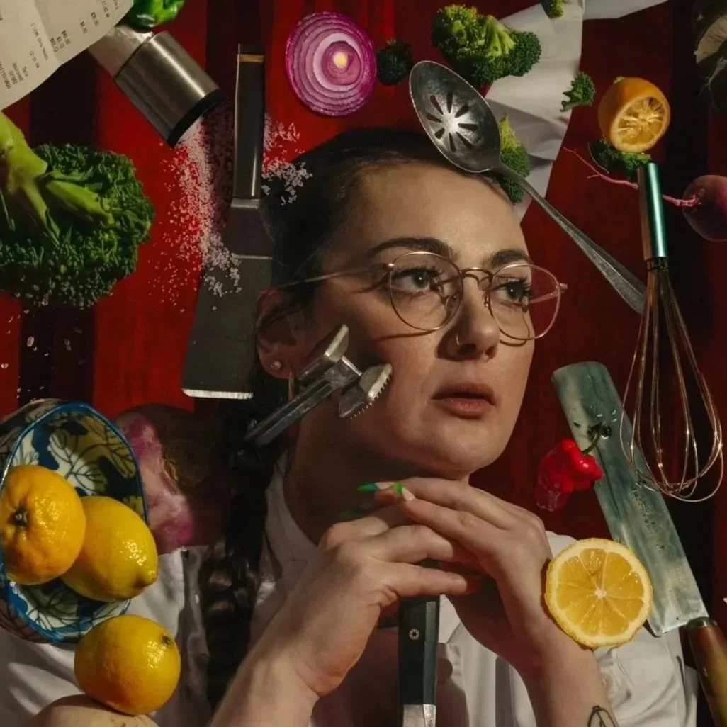 Chef Jessical Baston with a pensive pose, photographed with various kitchen instruments and vegetables and fruits in a very artful way