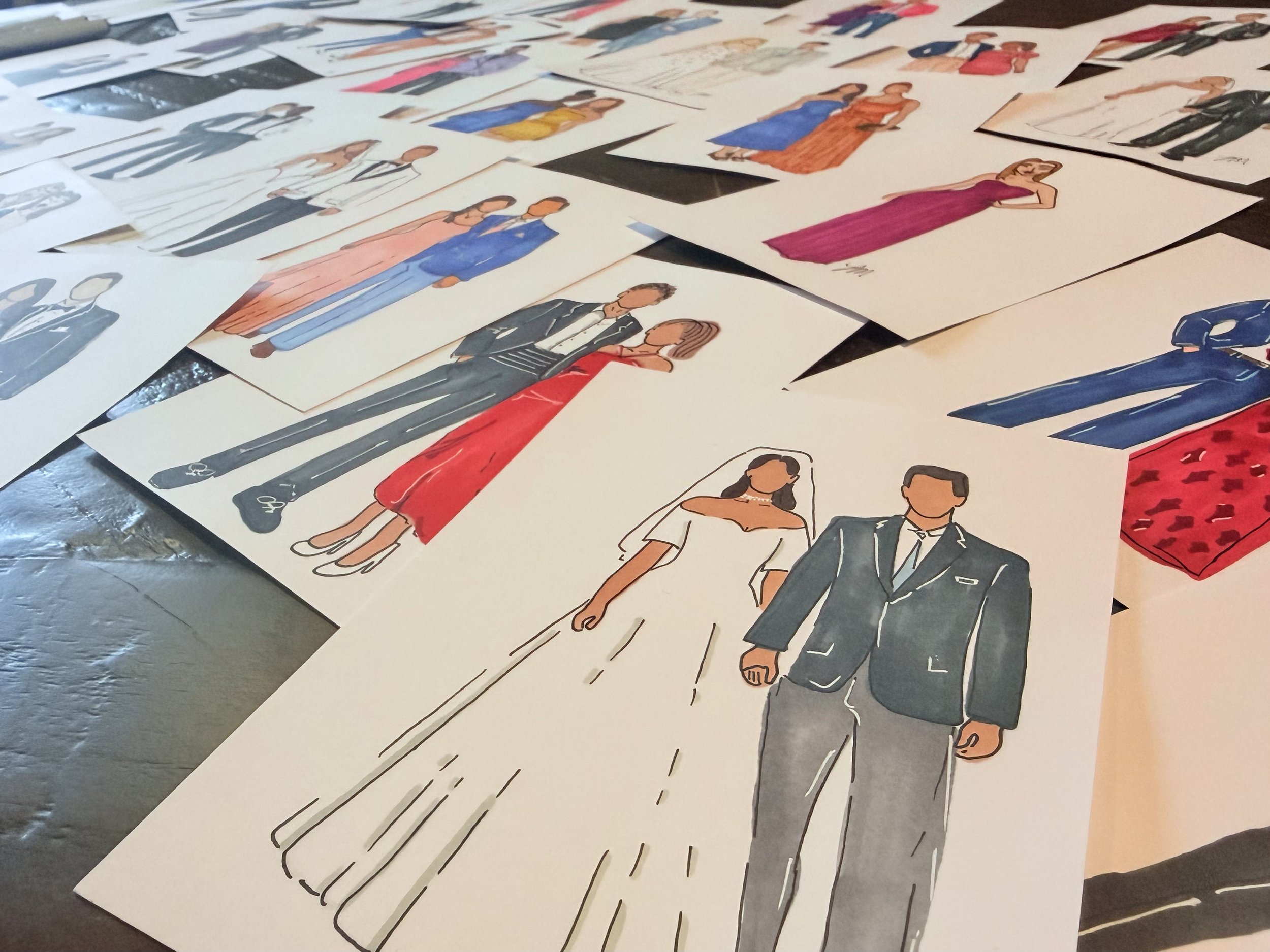 Collection of fashion sketches of various outfits and models, including formal wear, evening dresses, casual clothing, and suits, laid out on a table.