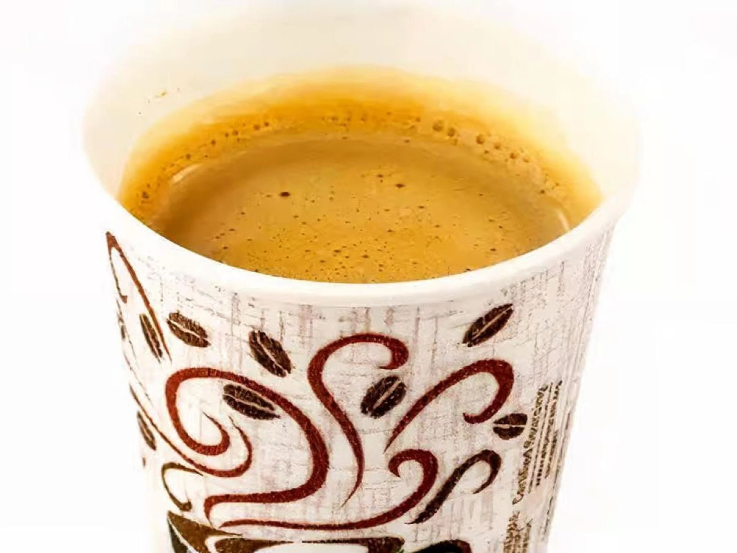 A white paper cup containing a hot beverage with a light brown foam and coffee streaks, with a decorative design on the outside.