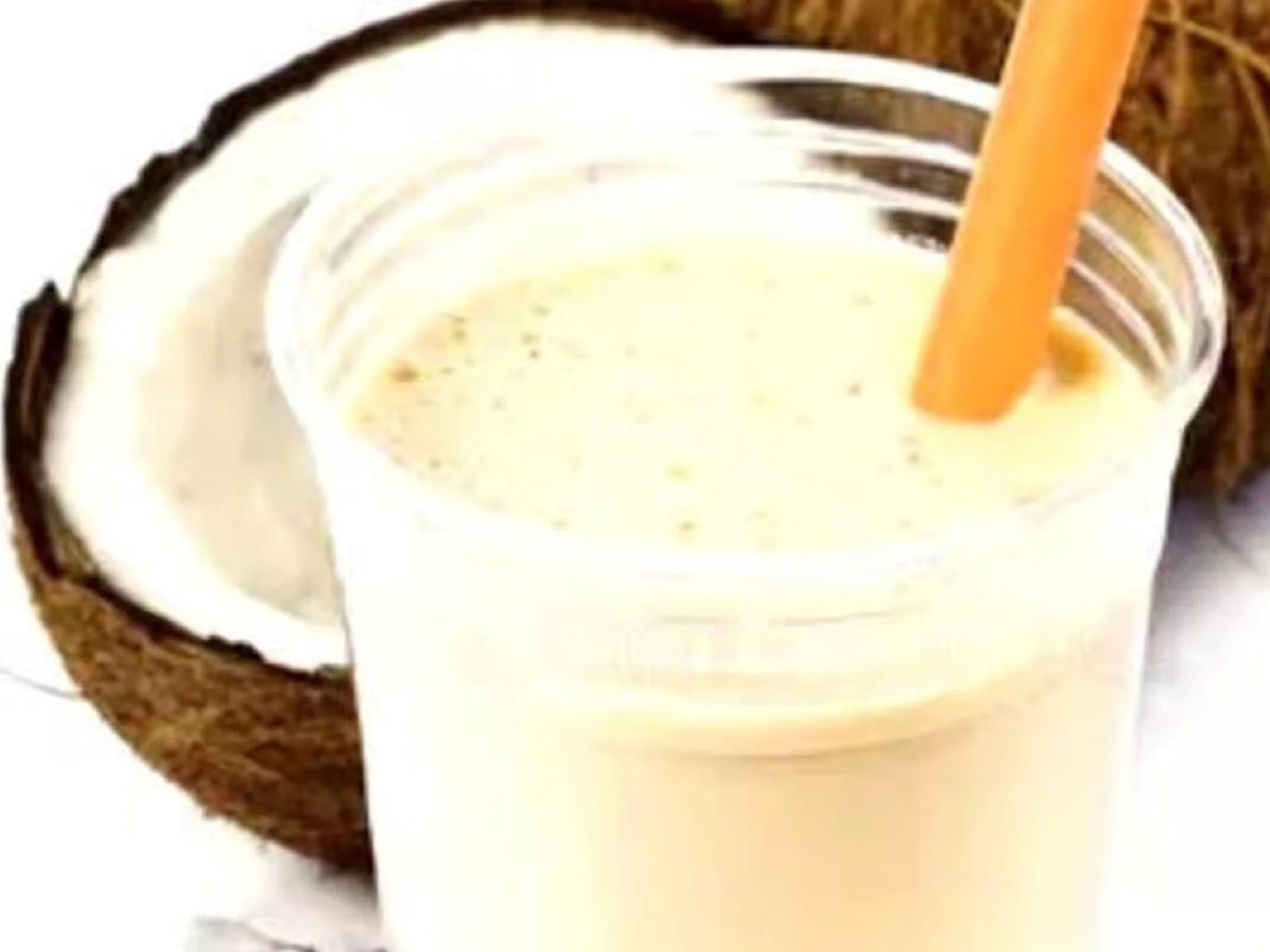 A glass of creamy, frothy beverage with a wooden straw, served alongside a coconut and sliced fruit.