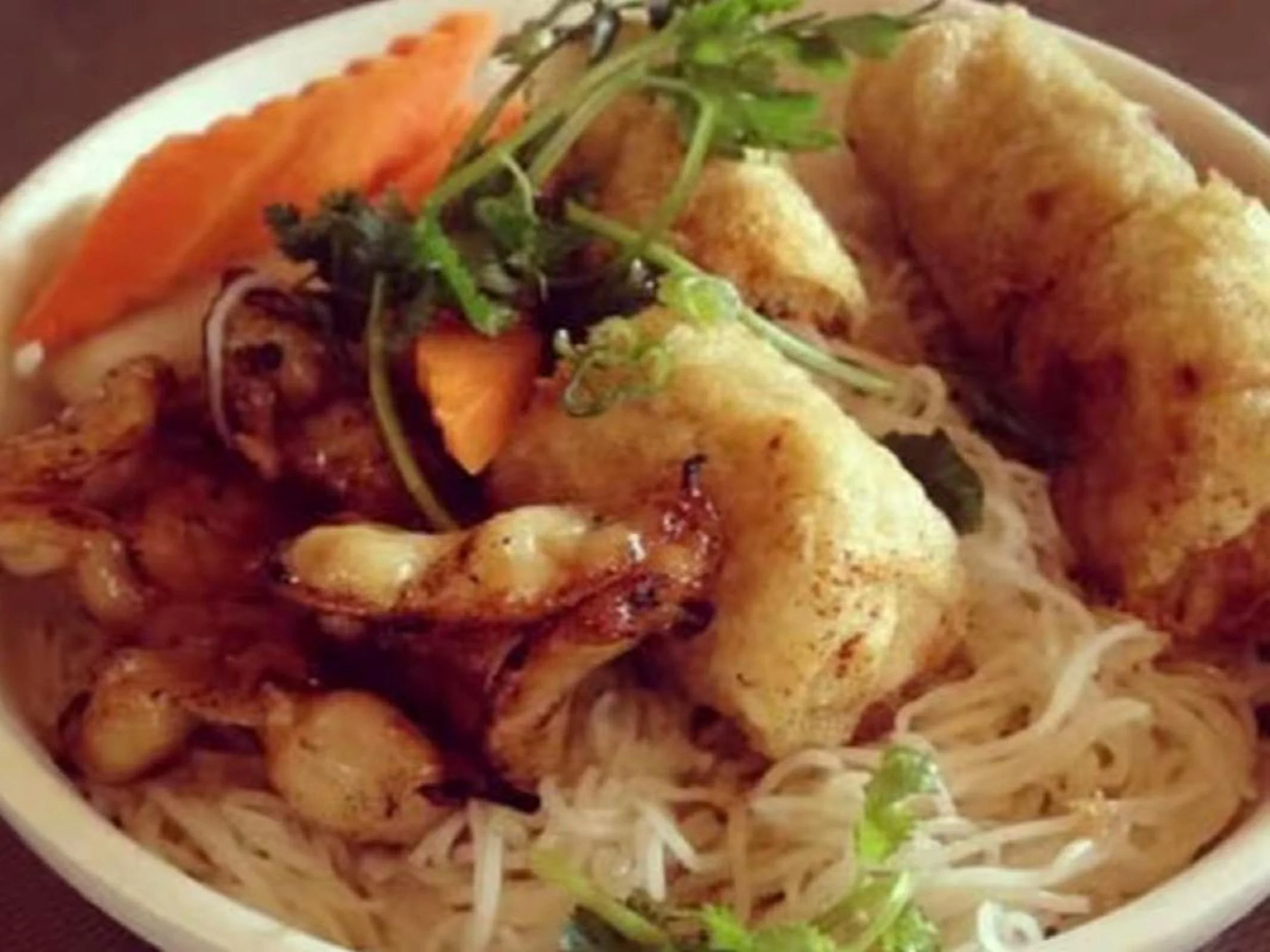 Bowl of Asian-style ramen noodles topped with fried chicken, fresh cilantro, sliced carrots, and bean sprouts.