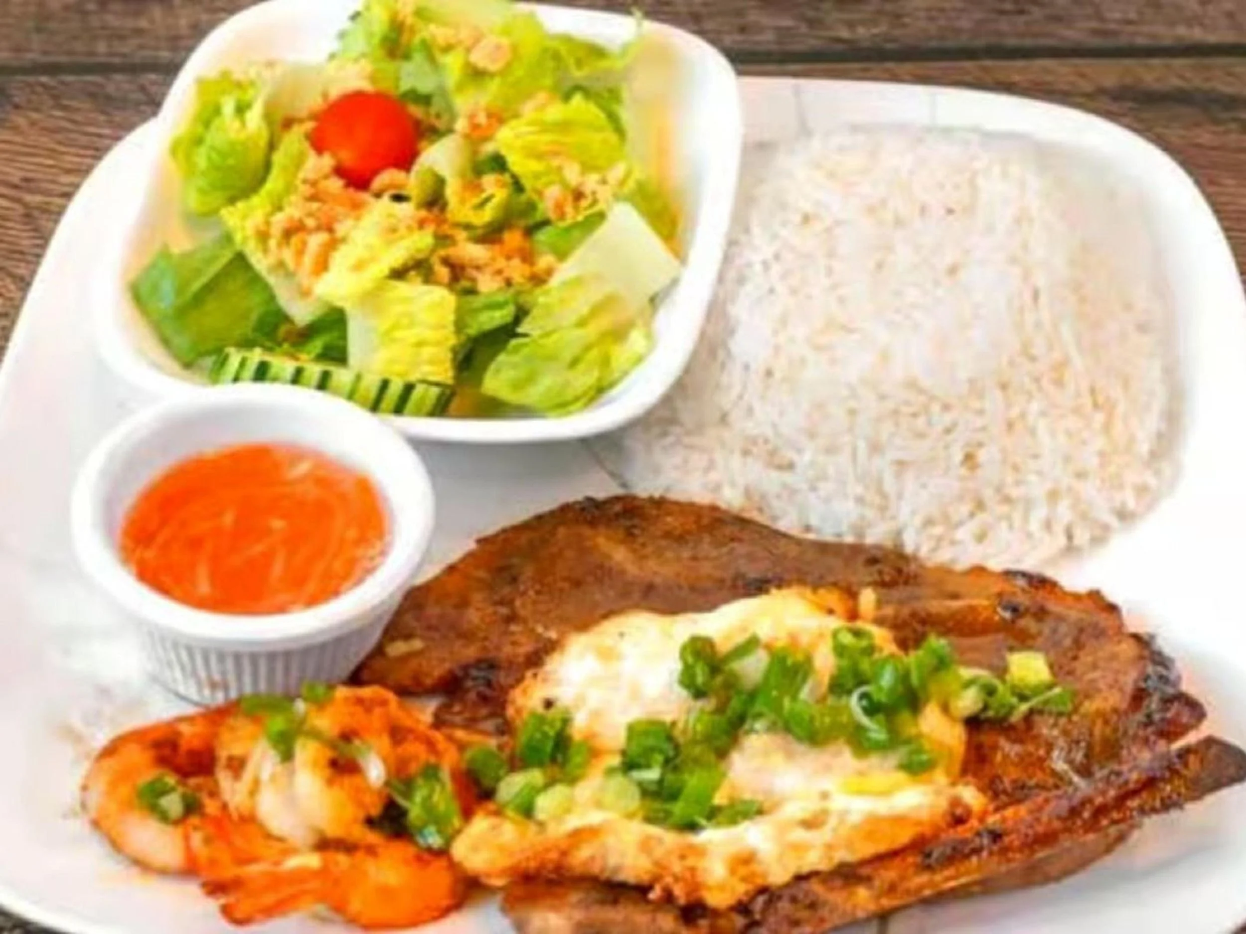 A plate of Vietnamese cuisine including grilled fish with fried egg, boiled shrimp, steamed rice, a side salad, and dipping sauce.