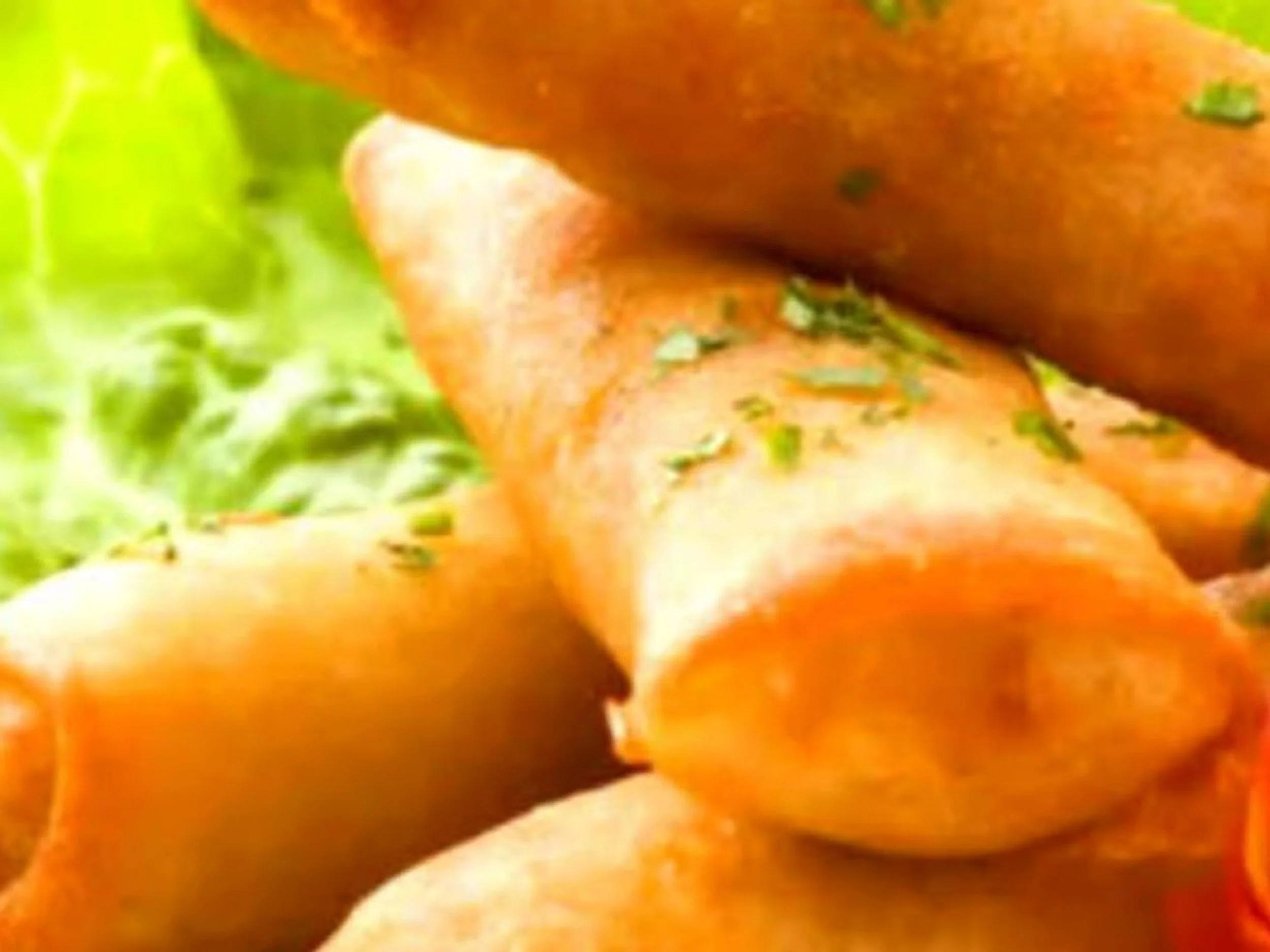 Close-up of a roasted chicken garnished with chopped herbs in front of leafy greens