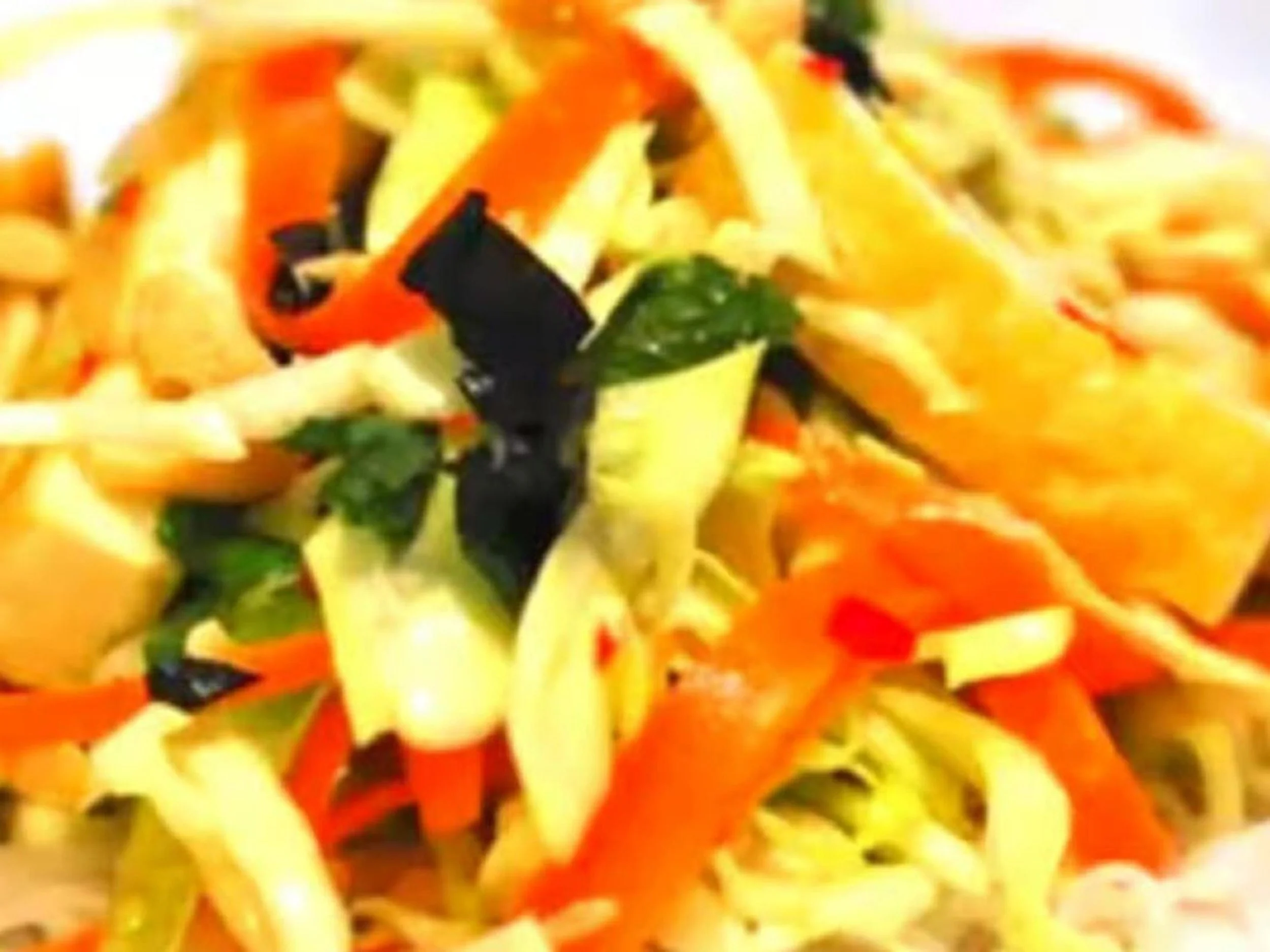 Close-up of a plate of shredded vegetables, including carrots, cabbage, and possibly zucchini, garnished with a basil leaf.