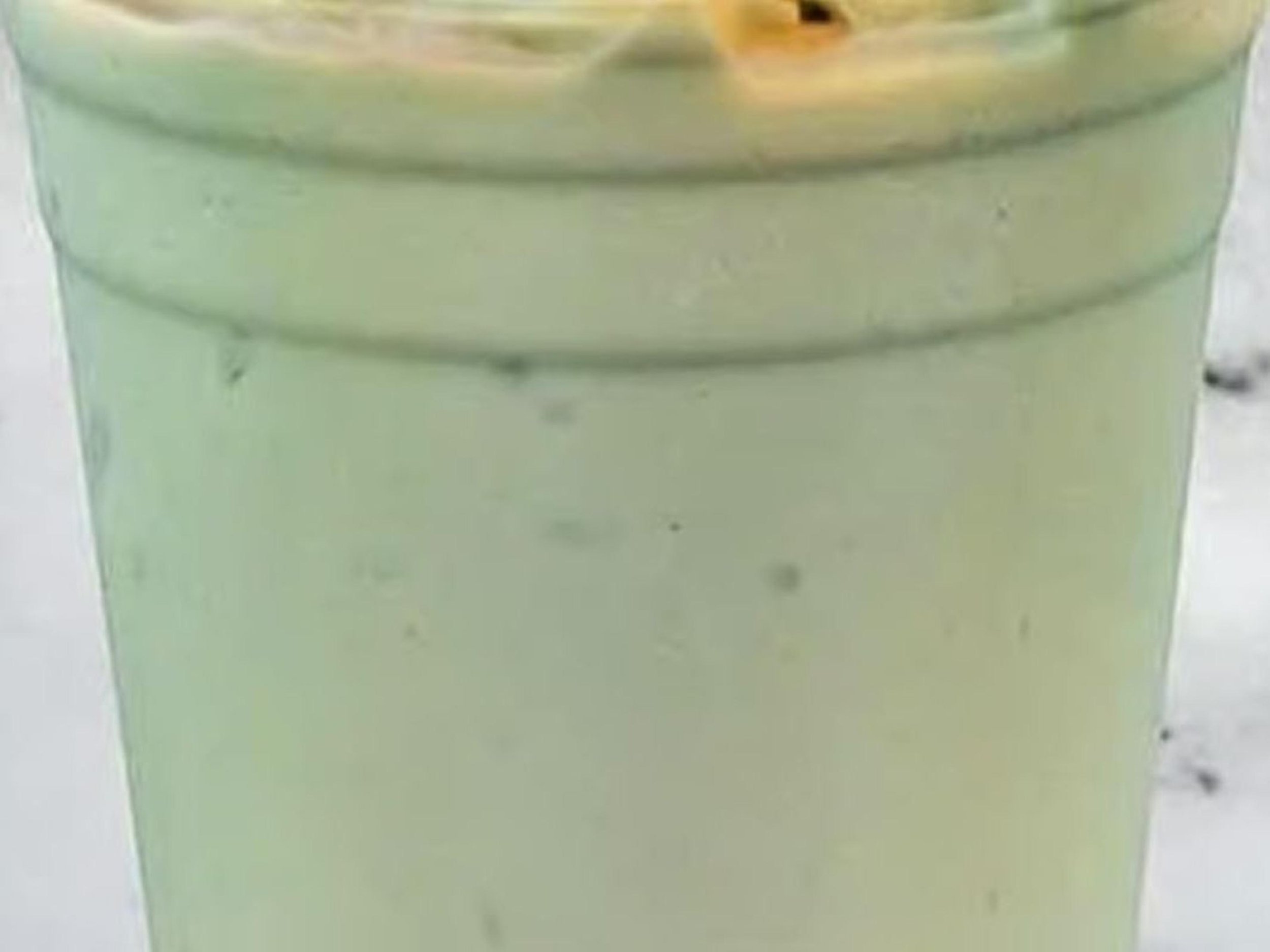Close-up of a glass with a yellowish-green beverage, possibly beer or cider, on a white surface.