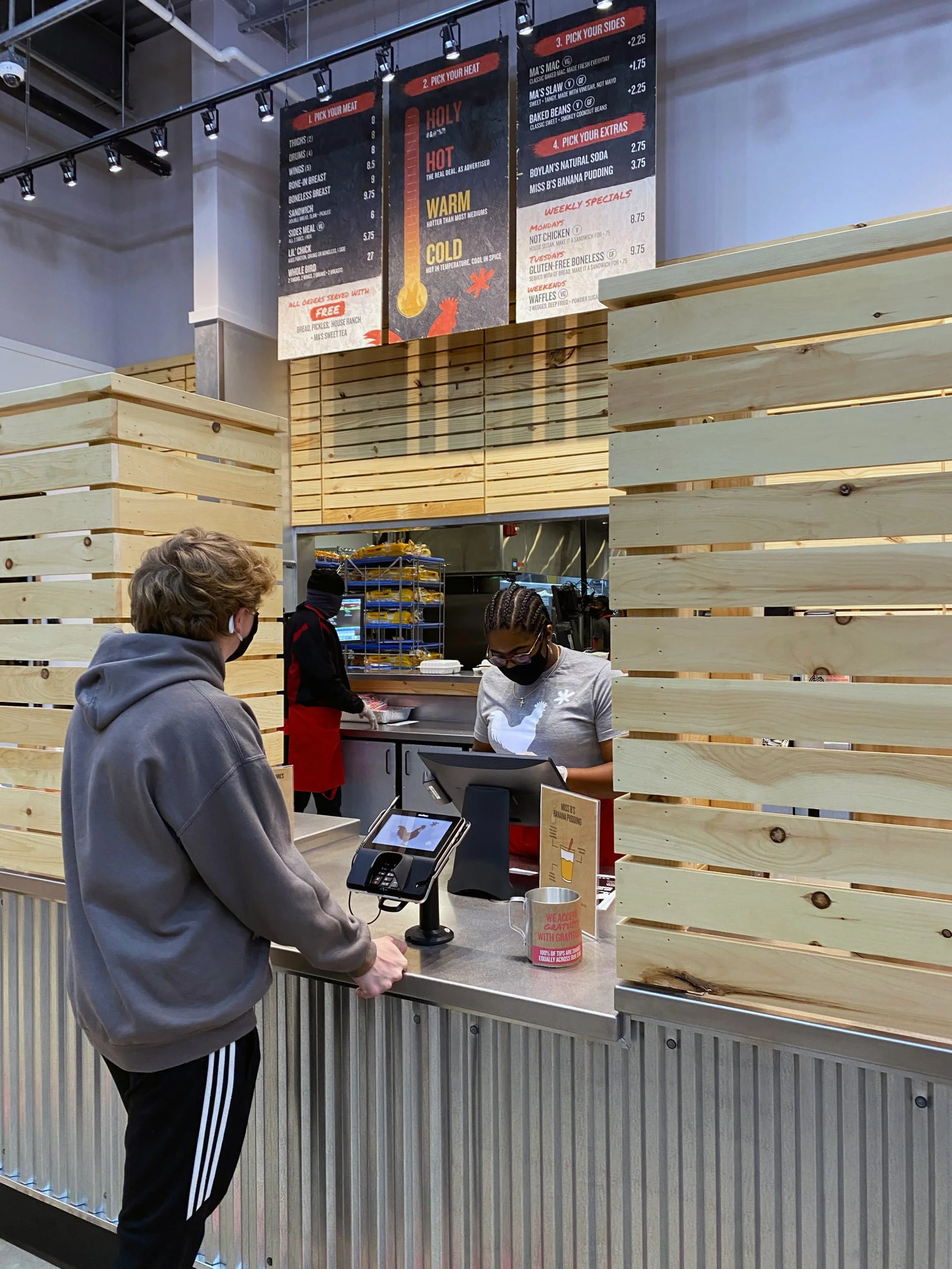A customer at a restaurant counter facing a staff member, with a menu board visible on the wall behind them.