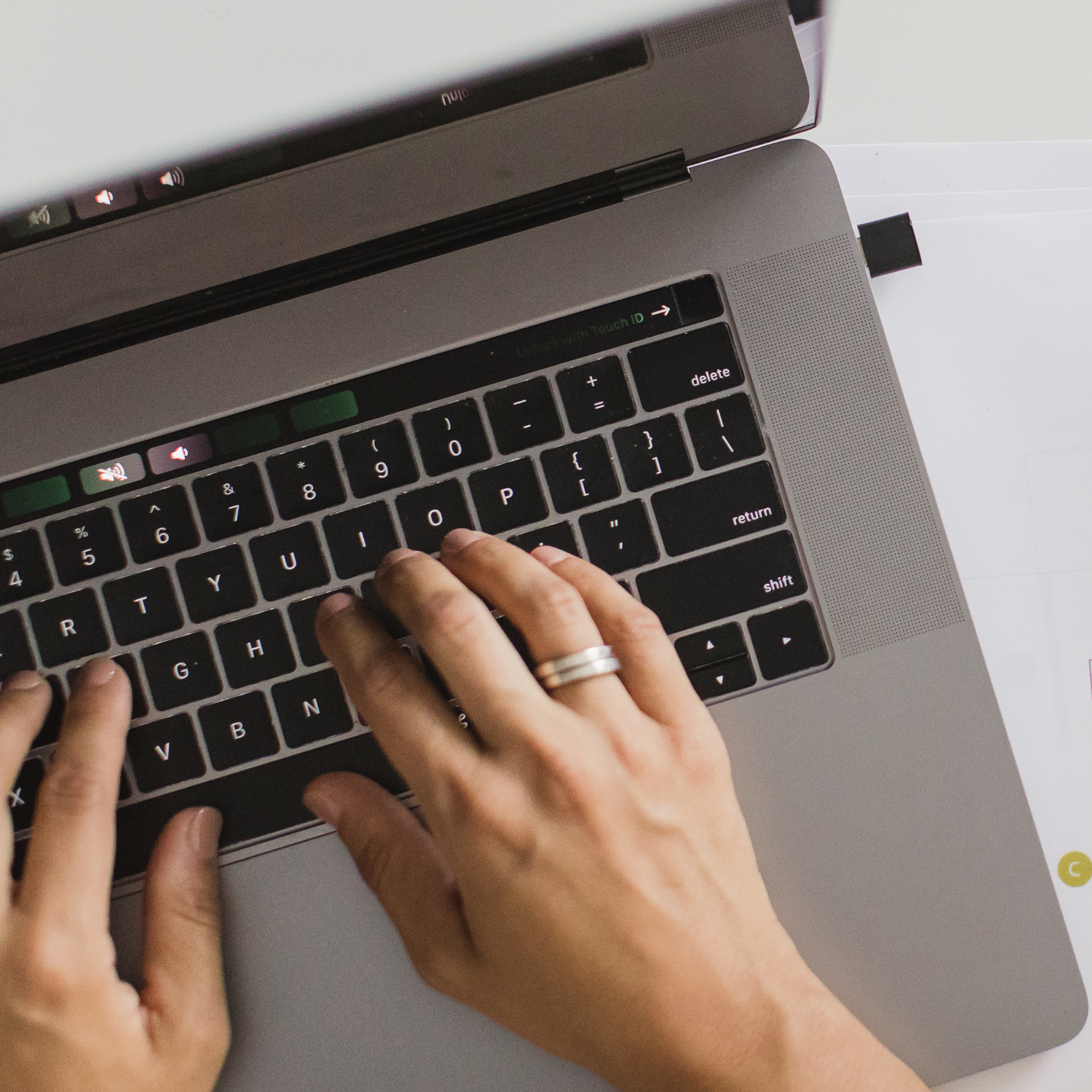 Close-up of hands typing on a silver laptop keyboard, with fingers positioned over the keys and a finger with a wedding ring visible.