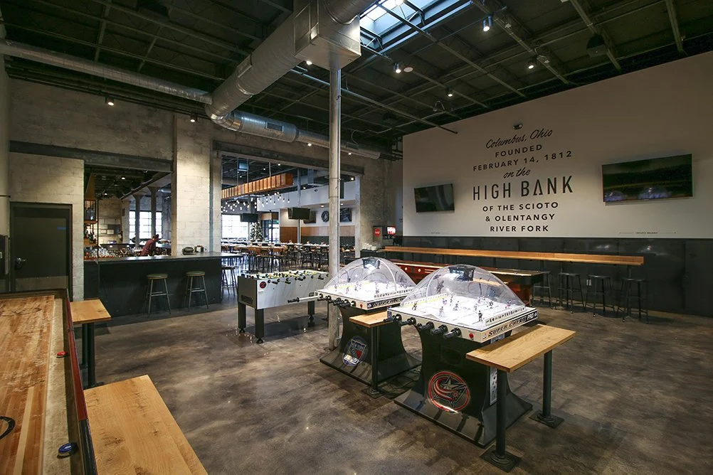 Interior of a game bar featuring bubble hockey tables and a wall painted with Columbus history.