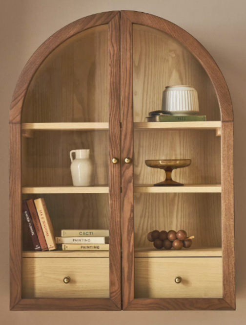 Wood wall-mounted display cabinet with glass doors and curated decorative home accessories.