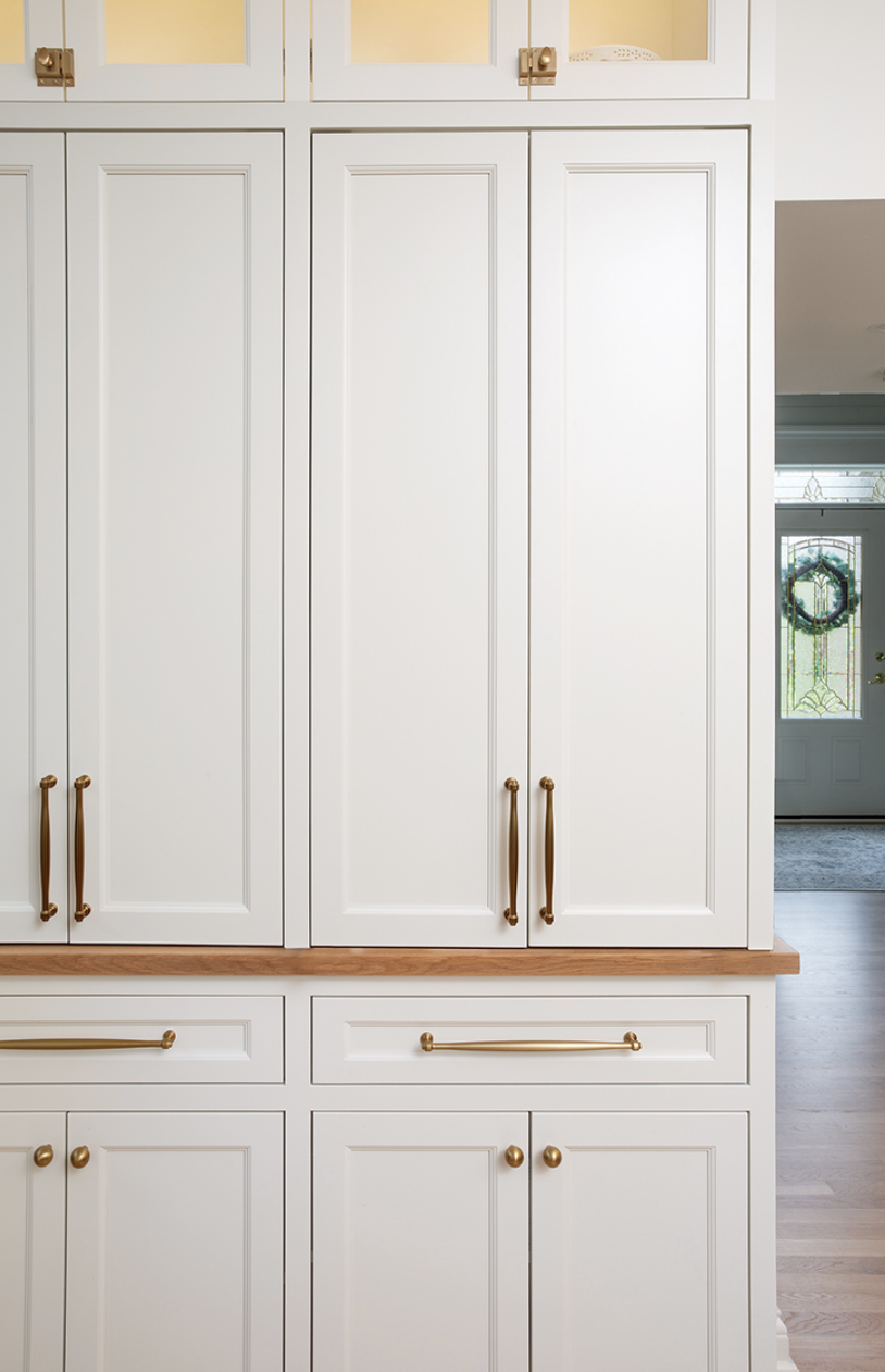 Floor-to-ceiling white kitchen cabinets with brass hardware and a wooden countertop.