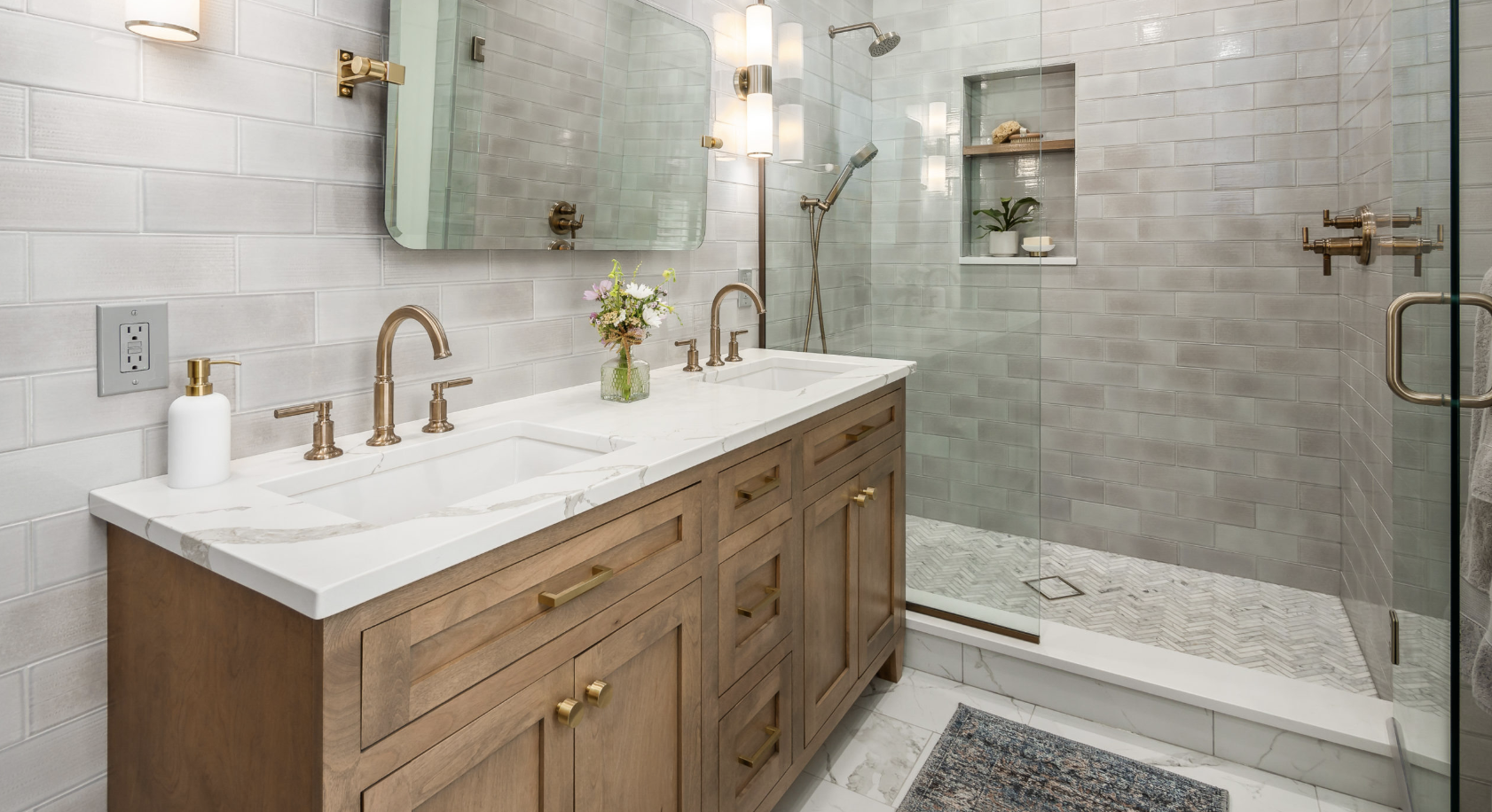 Double vanity with a stone countertop and brass fixtures beside a glass-enclosed walk-in shower.