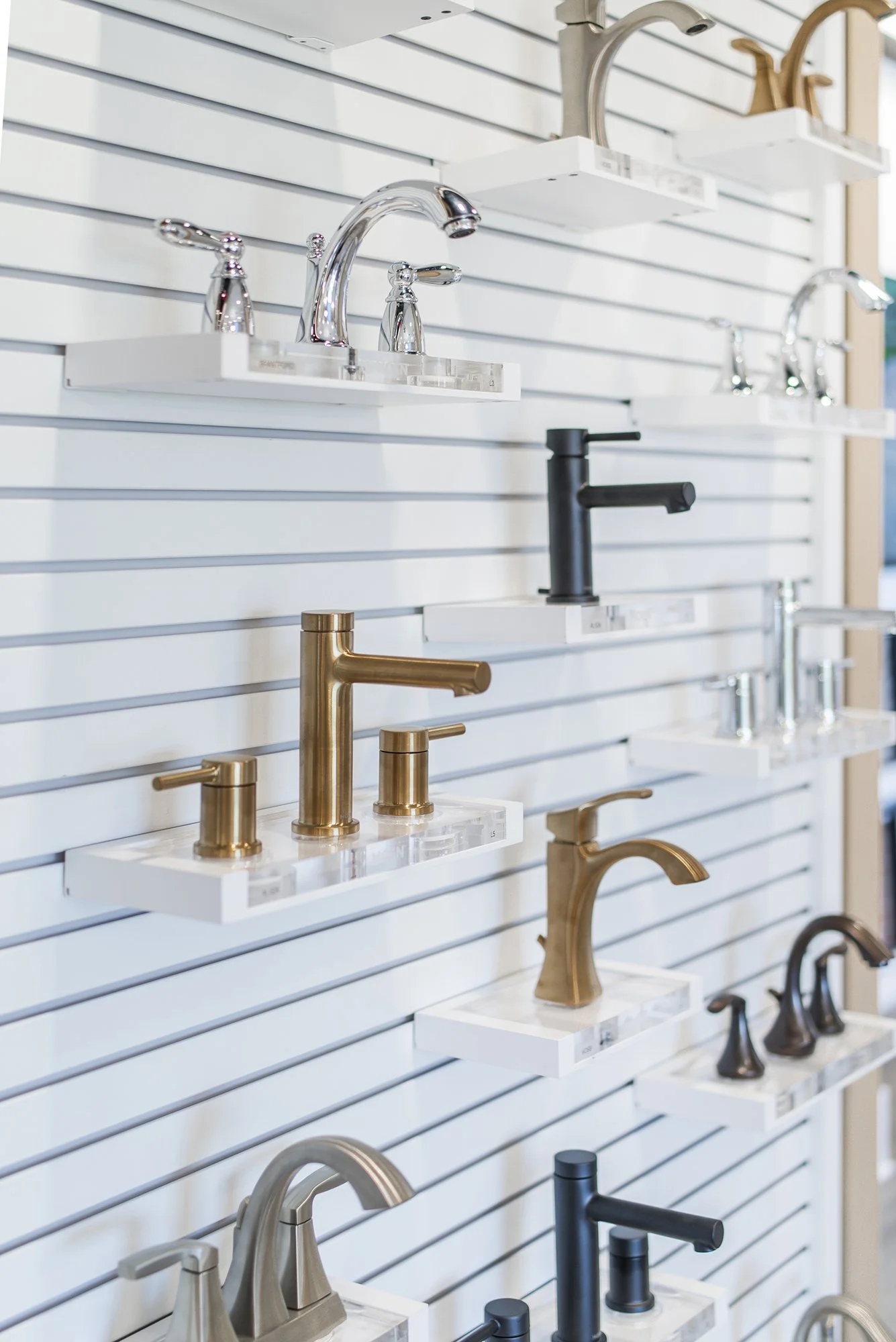 A display of various bathroom faucets in different finishes mounted on white shelves.