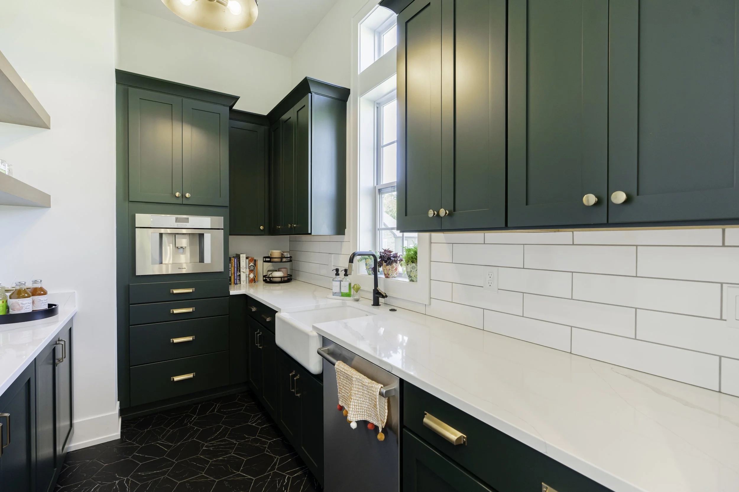Modern kitchen with dark green cabinets, white countertops, a farmhouse sink, and a window letting in natural light.
