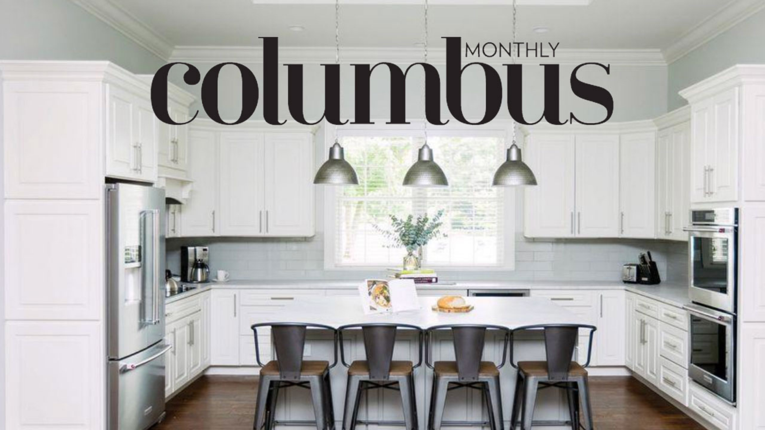 Bright kitchen with white cabinets, stainless steel refrigerator, and hanging pendant lights above a white dining table with black chairs.