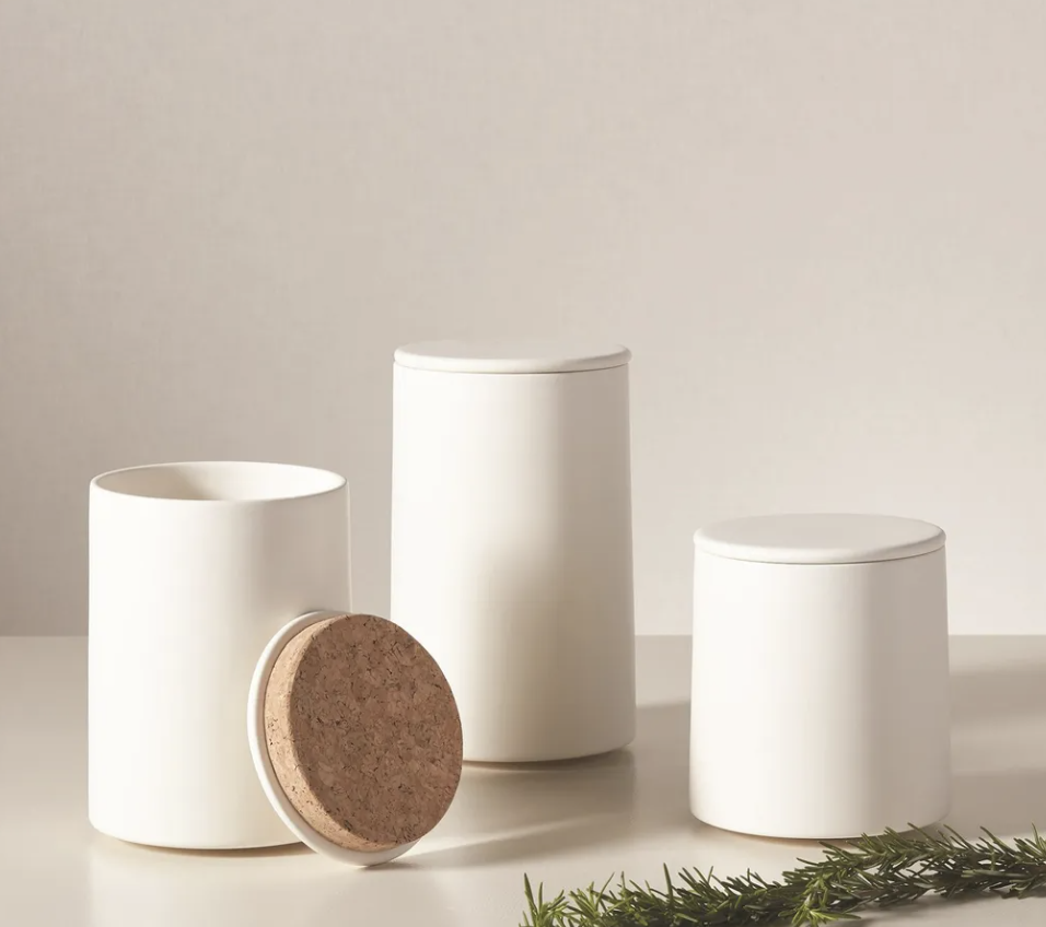 Minimalist white storage containers with cork detailing and natural greenery.