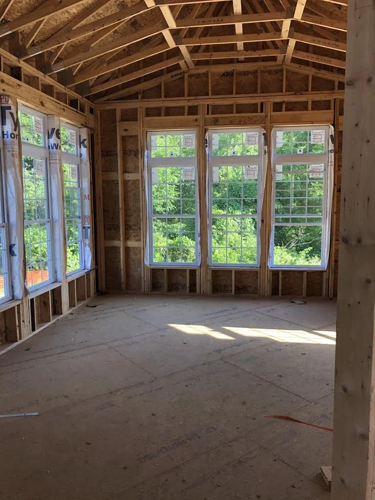 Interior of a room under construction with exposed wooden framing and multiple installed windows.