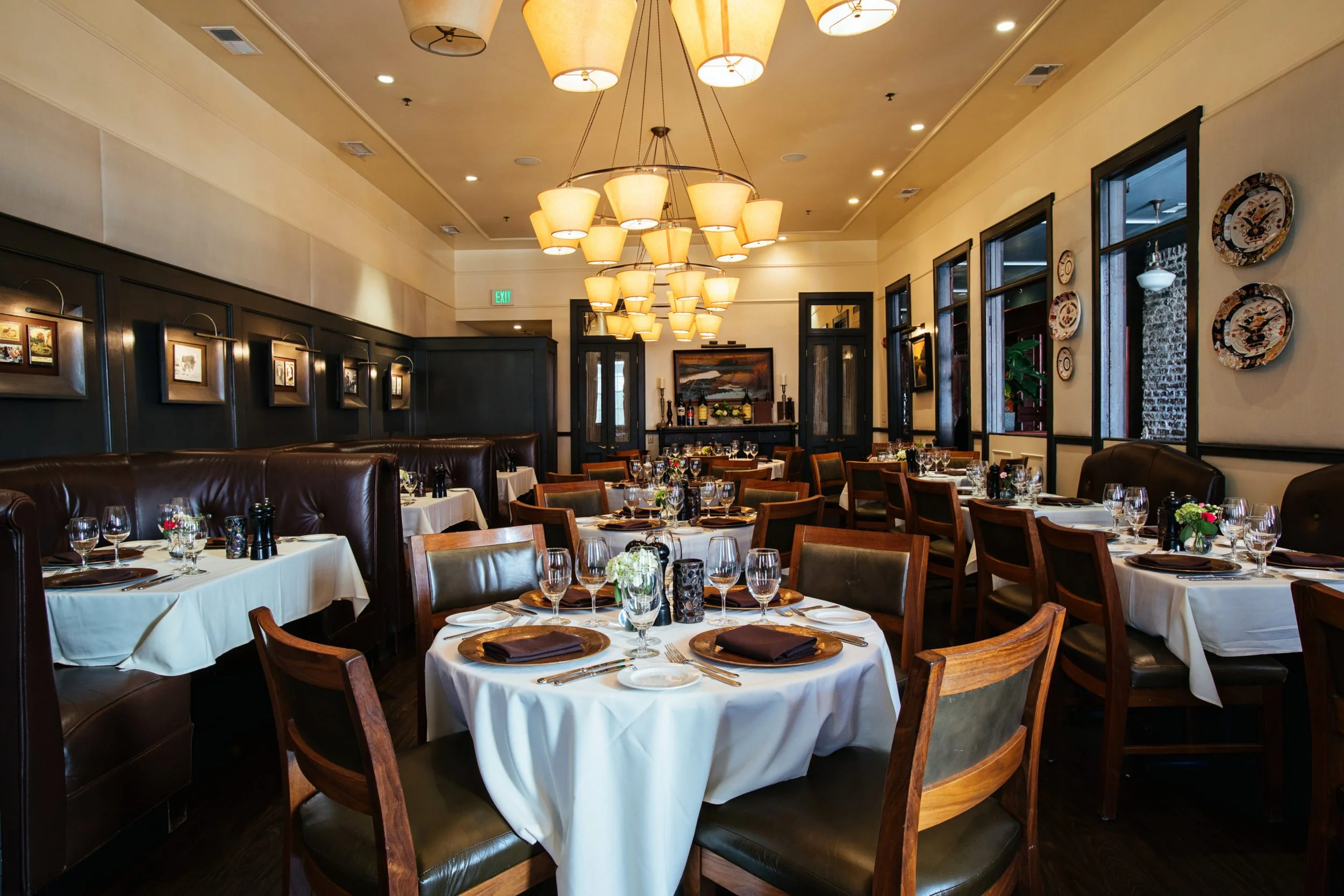 Dining room of a restaurant with white-clothed tables, dark wood chairs, and tiered chandeliers.