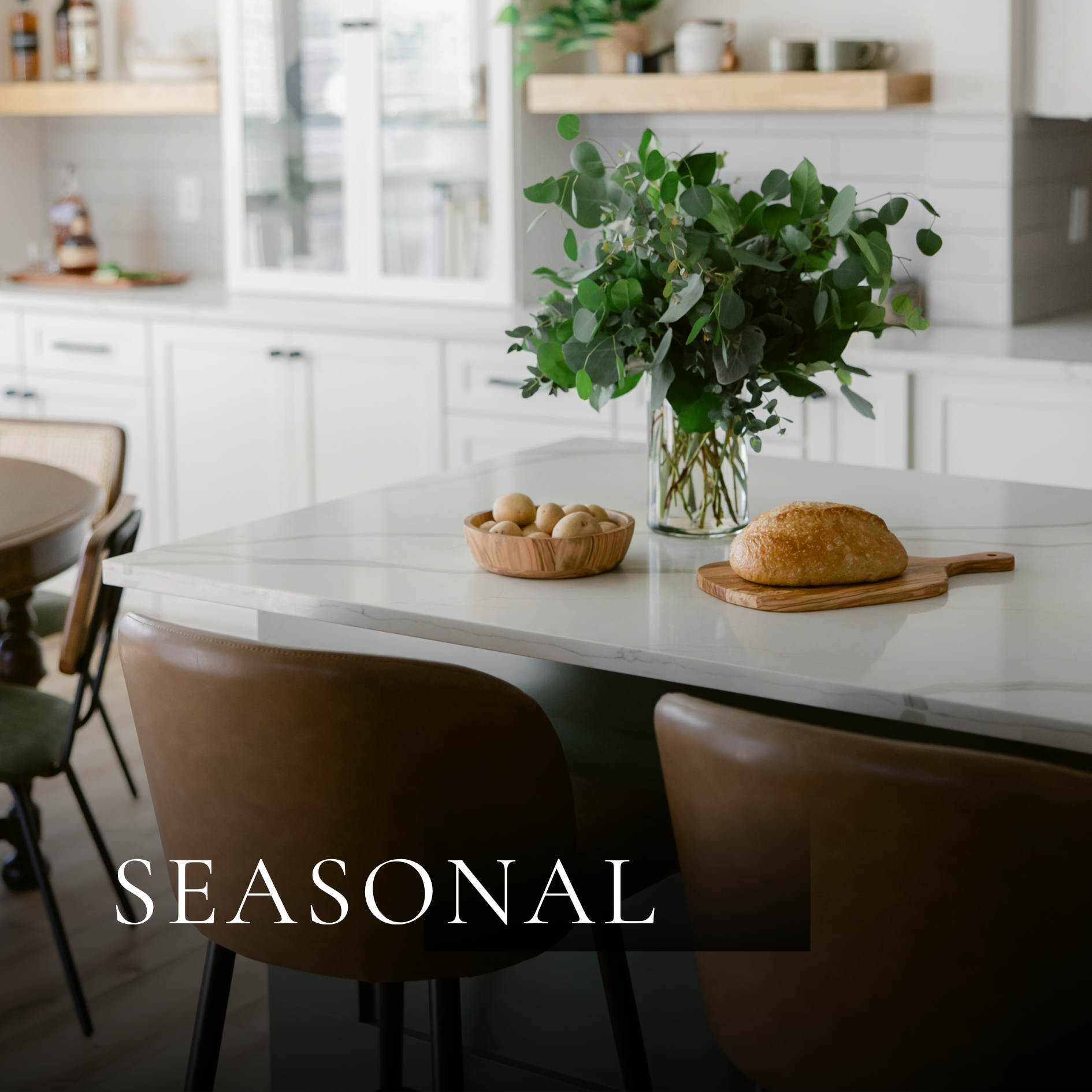Styled kitchen interior featuring white cabinetry, open wood shelving, natural greenery and curated countertop decor.