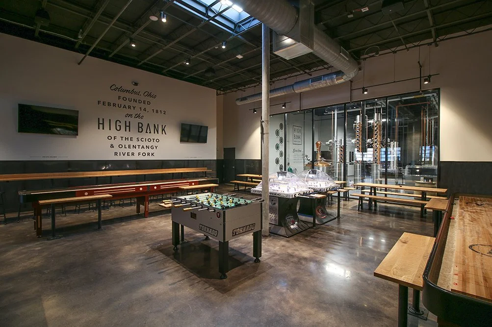 Interior of High Bank Distillery with game tables, shuffleboard, and a view of the production area through glass walls.