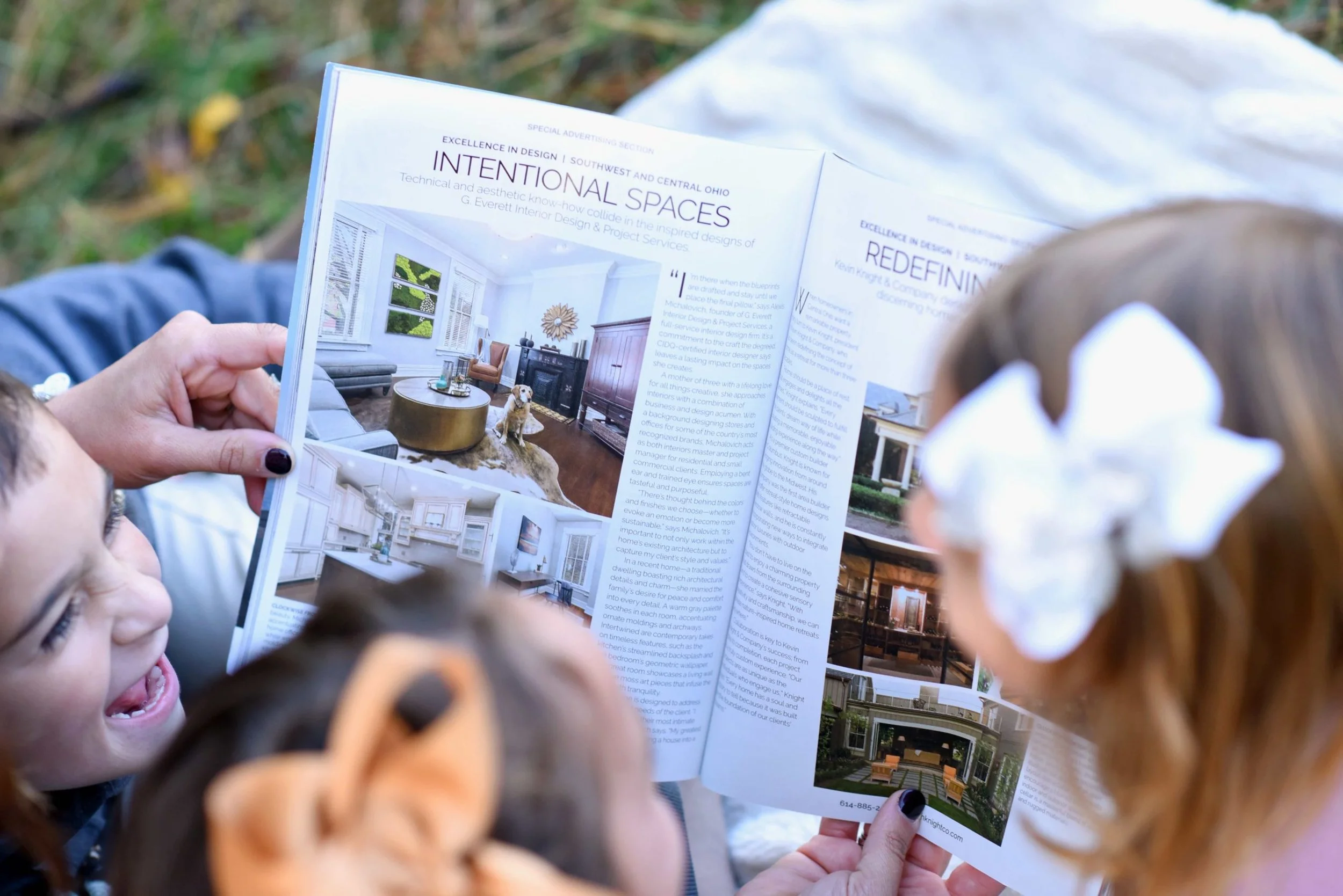 Two children looking at an open interior design magazine held by an adult.
