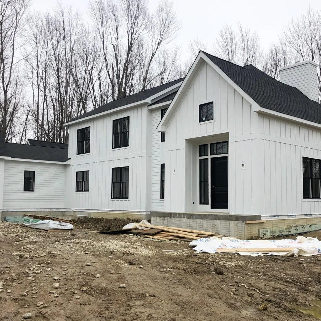 A newly constructed white house with black window frames and a black roof, set against a background of bare trees.