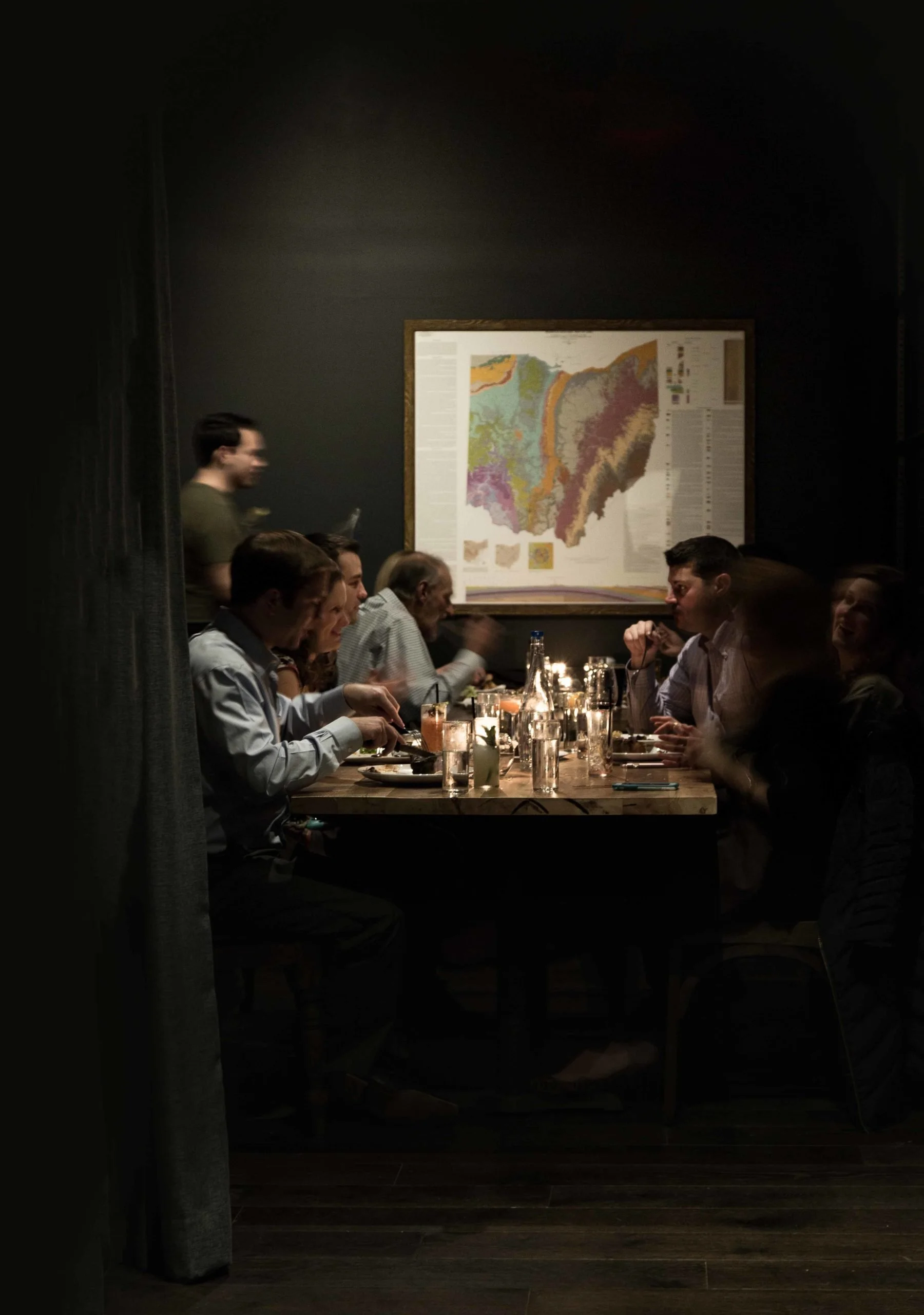 A group of people dining at a table in a dimly lit restaurant, with a large geological map hanging on the wall.