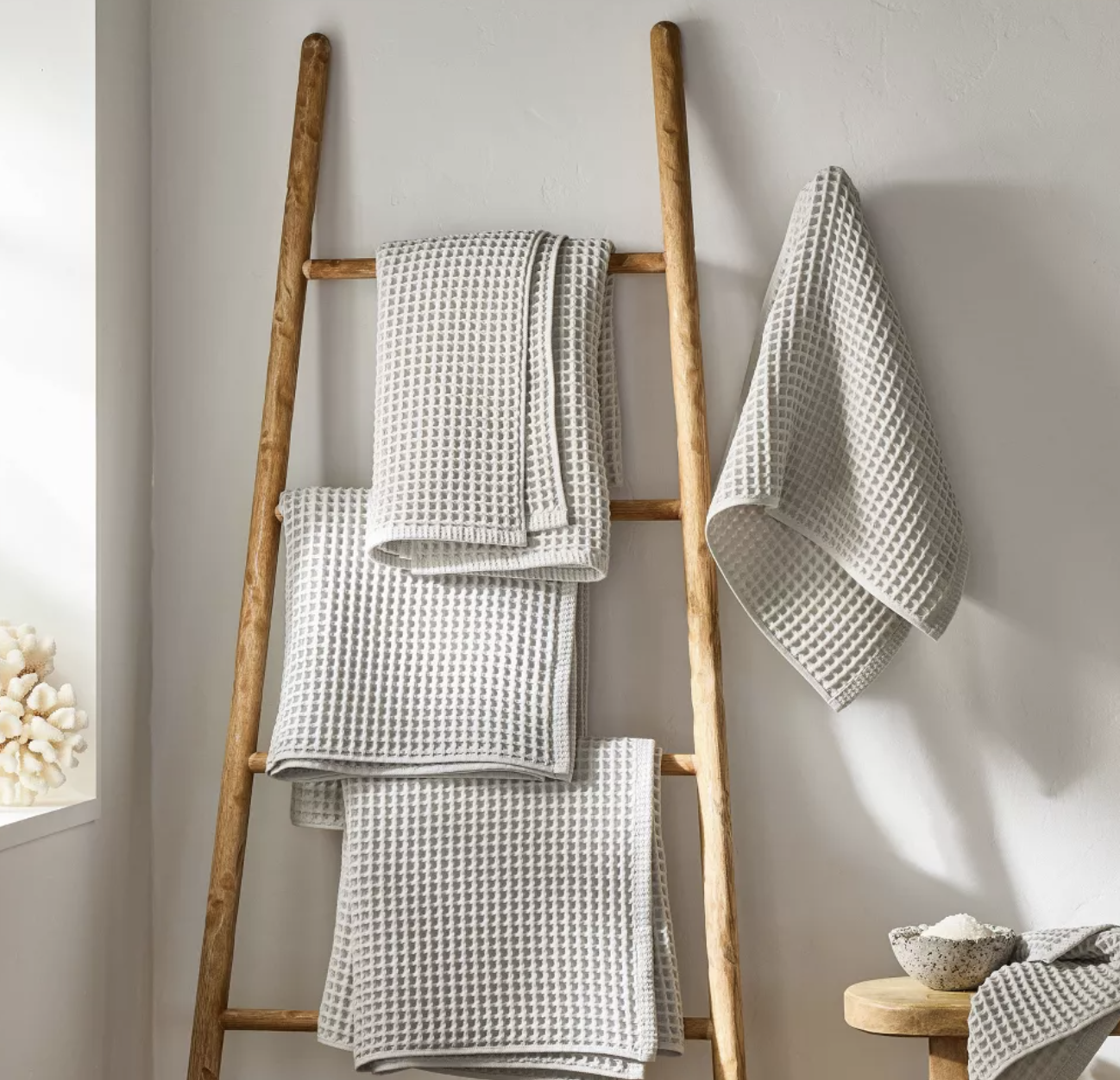 White textured bath towels displayed on a natural wood ladder in a neutral bathroom.