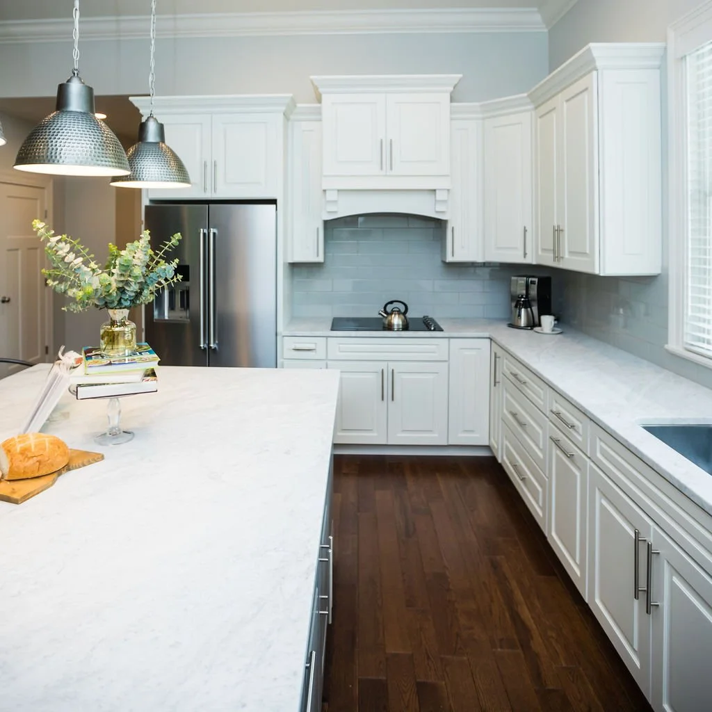 Modern kitchen with white cabinets, a marble-topped island, and a stainless steel refrigerator.