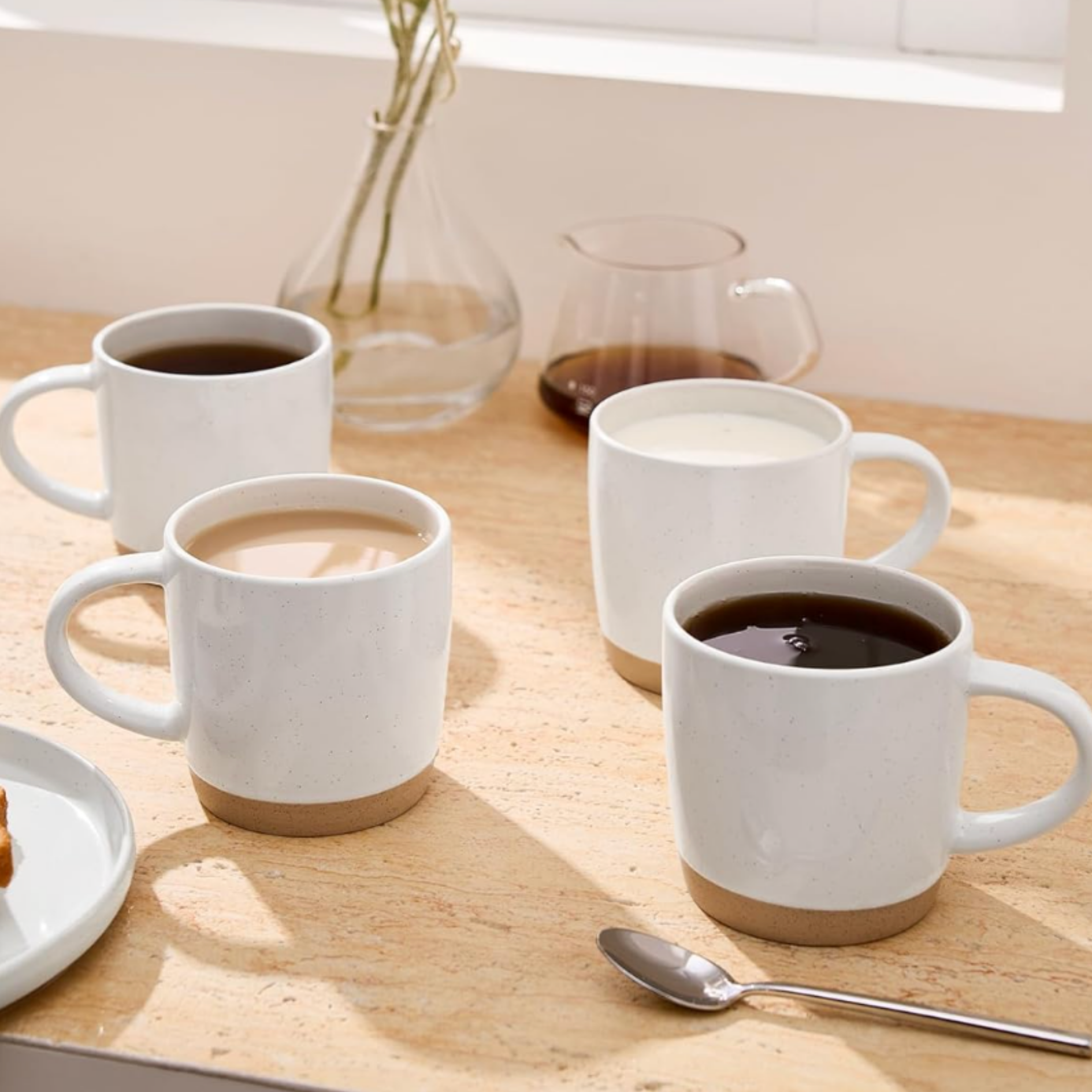 White ceramic coffee and tea cups styled on a wood table with dried florals and glass serveware.