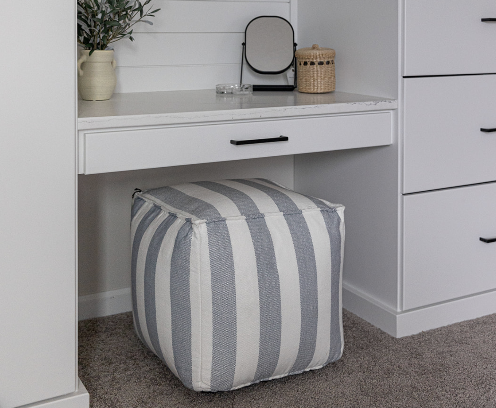 A blue and white striped fabric pouf tucked under a white built-in vanity.