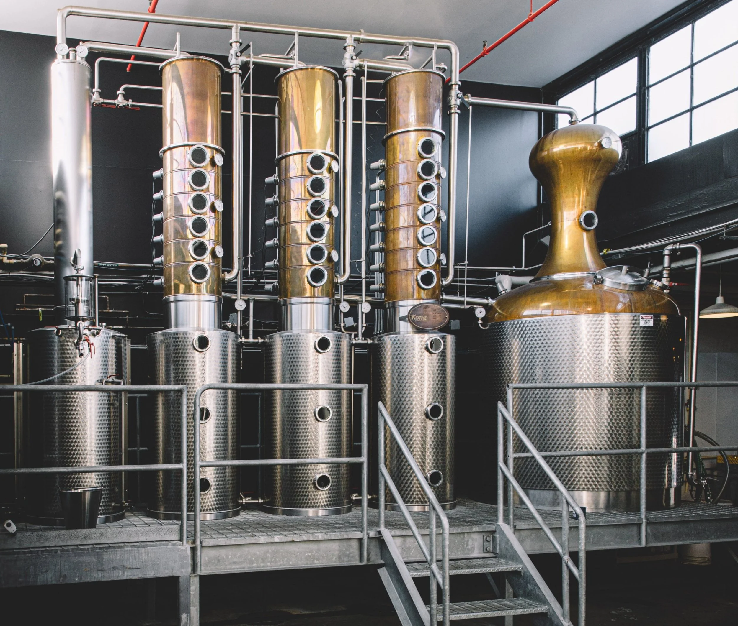 Industrial distillery equipment with copper columns and stainless steel vats on a metal platform.