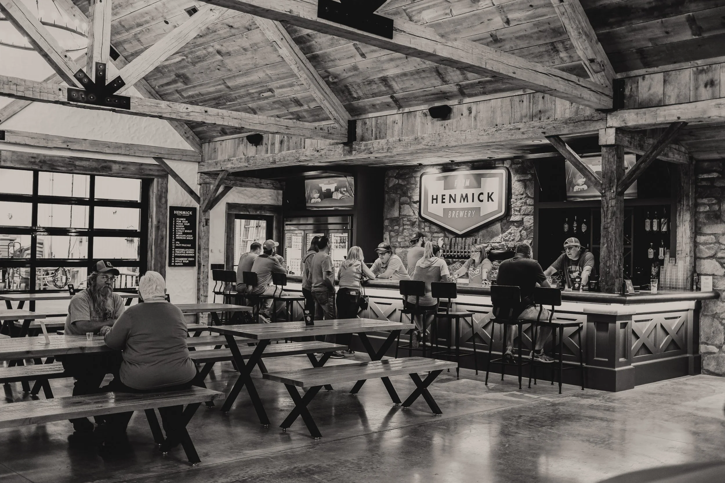 Interior of a wooden-framed brewery with a long bar, patrons sitting on stools, and a large Henmick Brewery sign.