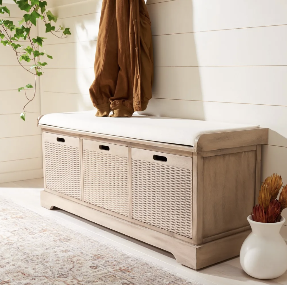 Entryway storage bench with white cushion, woven baskets, greenery and wall hooks.