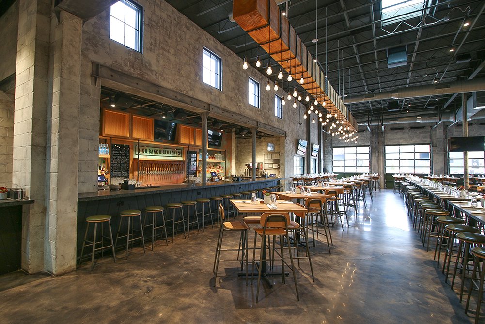 High Bank Distillery bar and dining area with high-top tables, bar stools, and industrial lighting.