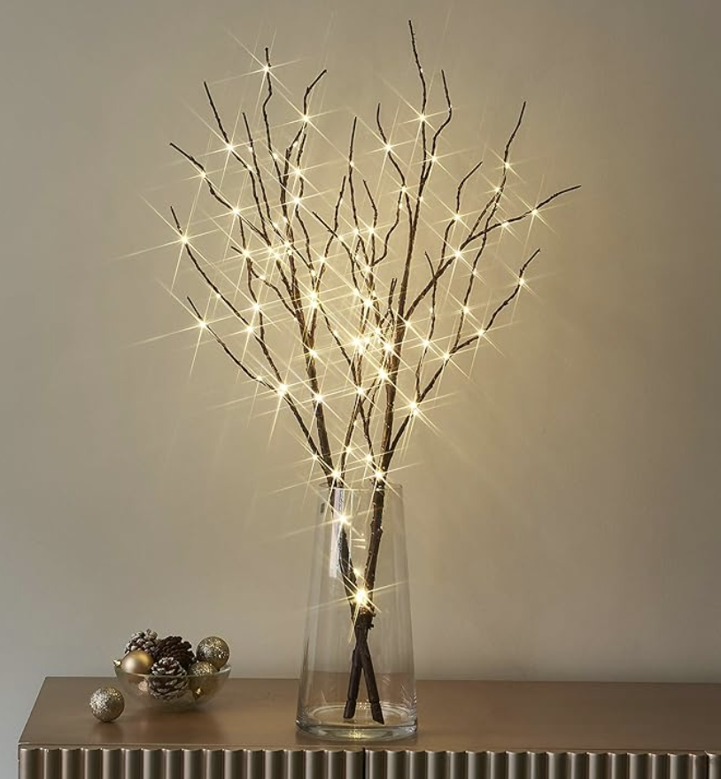 Holiday branch arrangement with string lights and Christmas ornaments in a clear glass vase.