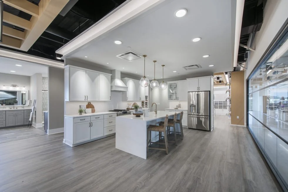 Modern kitchen with white cabinets, a central island with three stools, and stainless steel appliances.