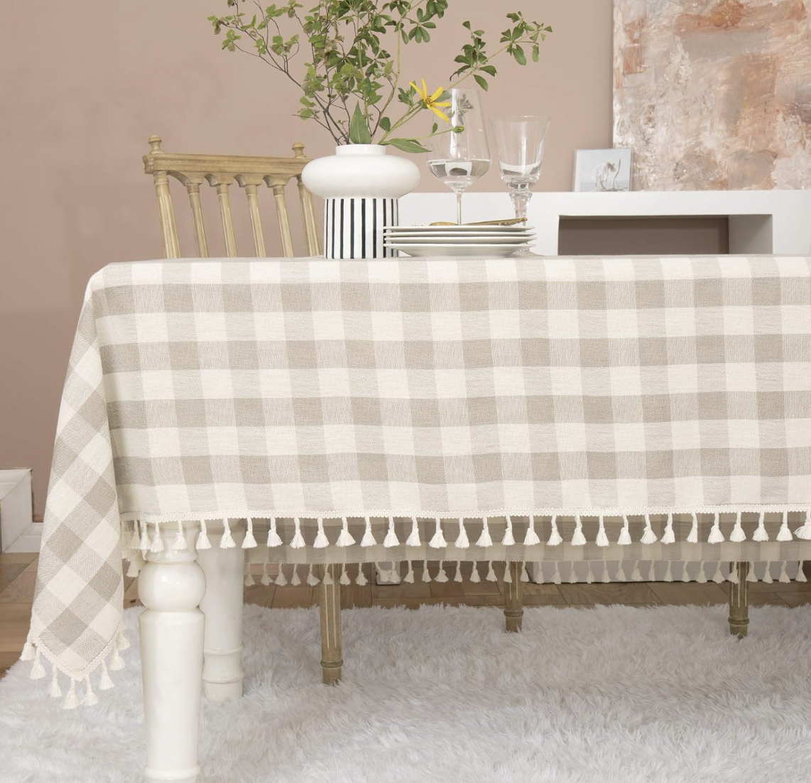 Curated dining table setting with checkered tablecloth, floral arrangement, wine glasses and layered dinnerware.