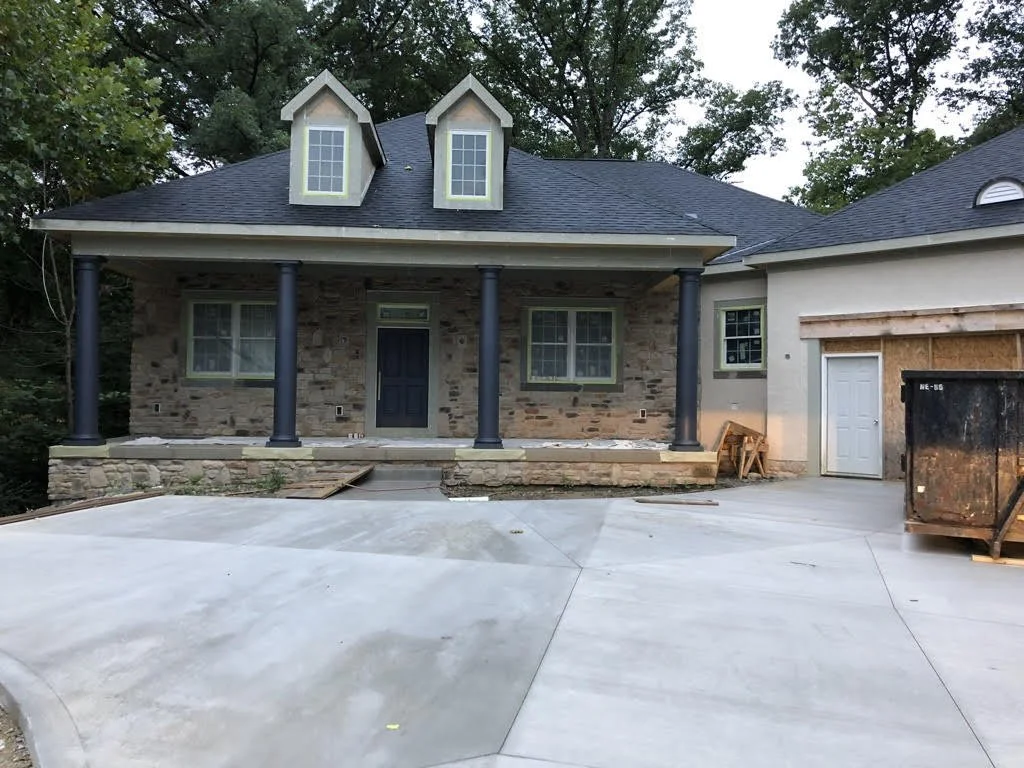 A stone-faced house under construction with a front porch, columns, and a concrete driveway.