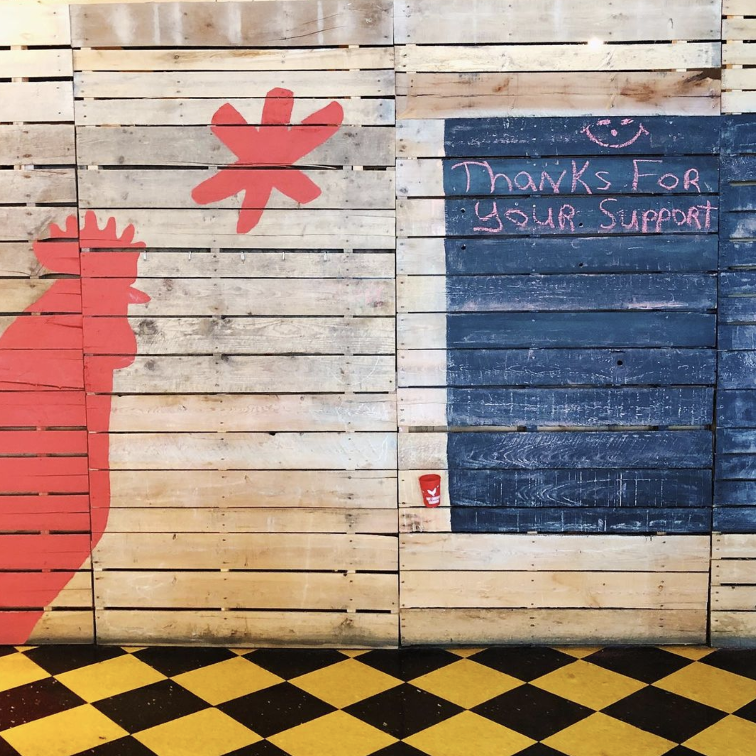 Wooden wall with a red rooster silhouette and a chalkboard sign reading “Thanks for your support.”.