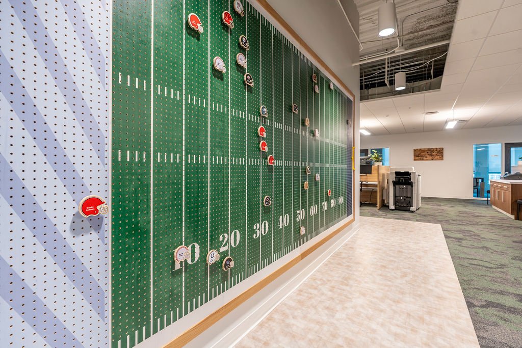 Indoor football-themed display board with football helmet tokens on it, resembling a football field with yard lines, in an office or recreational area.