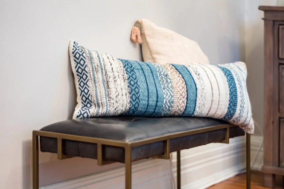 A long, blue and white patterned lumbar pillow sits on a dark bench, with a smaller neutral pillow behind it.