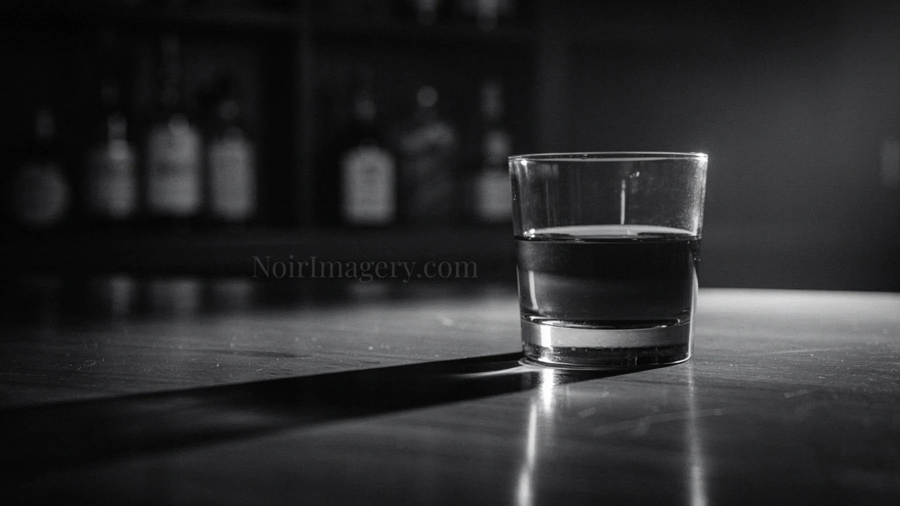 Black and white noir image of a drinking glass on a table with strong directional light and deep shadows