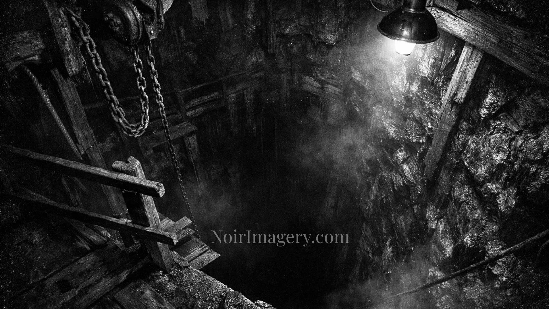 Atmospheric black-and-white image of a dark abandoned mine shaft with chains, mist, and wet rock walls.