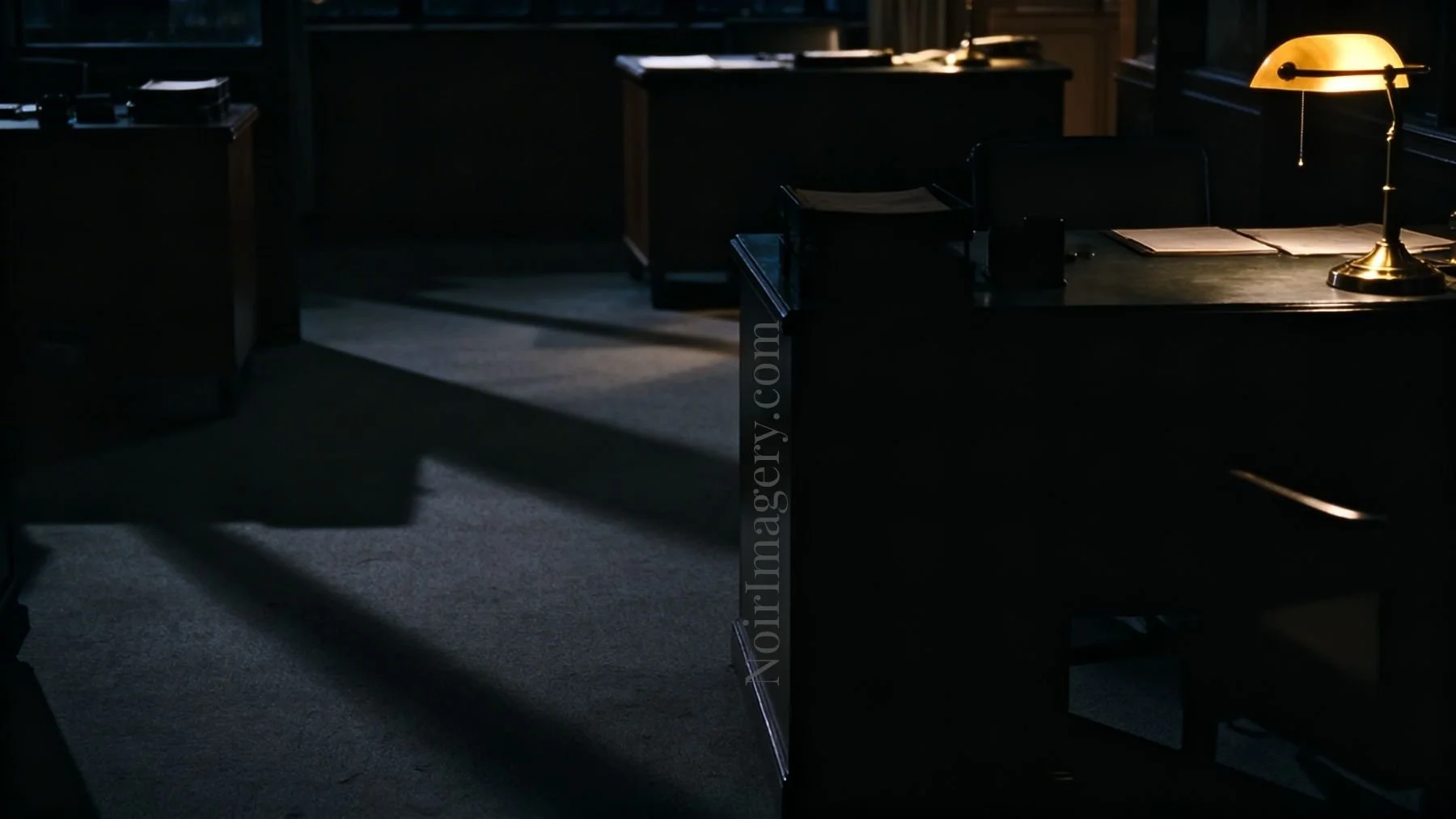 An empty office interior with desks and long shadows cast across the floor, moody noir lighting.