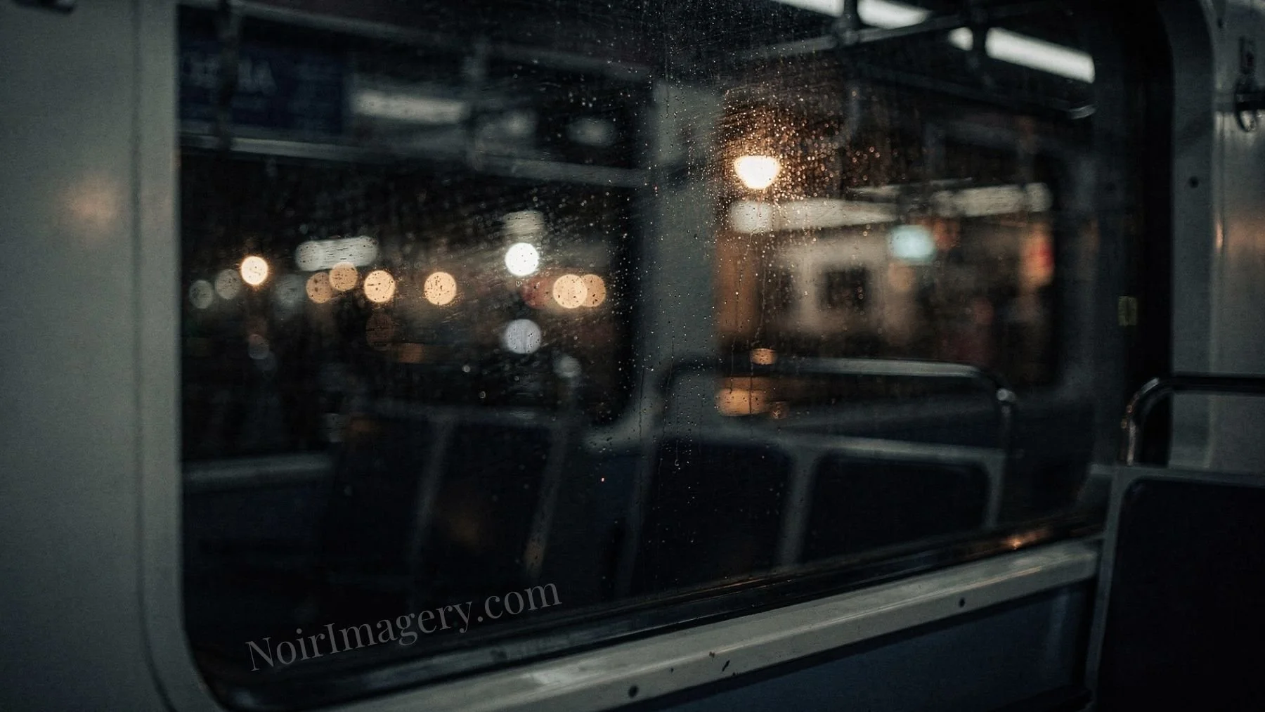 Rain-speckled train window reflecting blurred station lights and empty seats