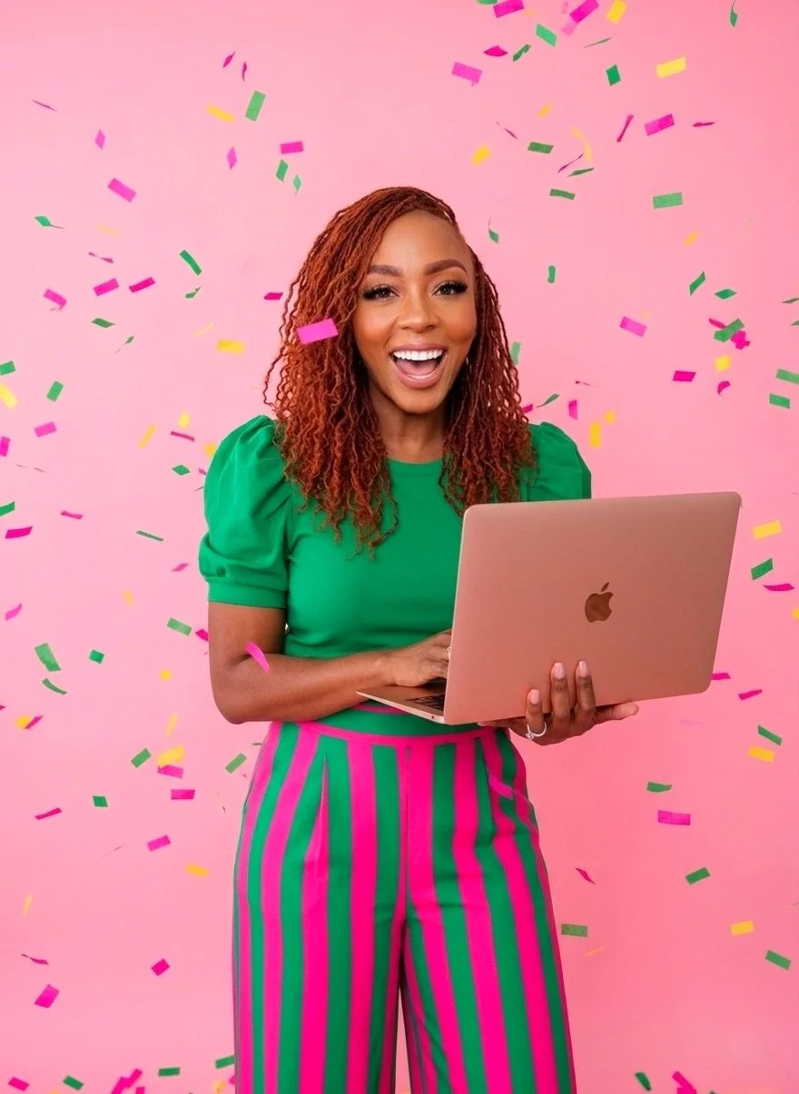 A woman with curly reddish hair in a green top and pink and green striped pants holding a gold MacBook laptop, celebrating with colorful confetti falling around her against a pink background.