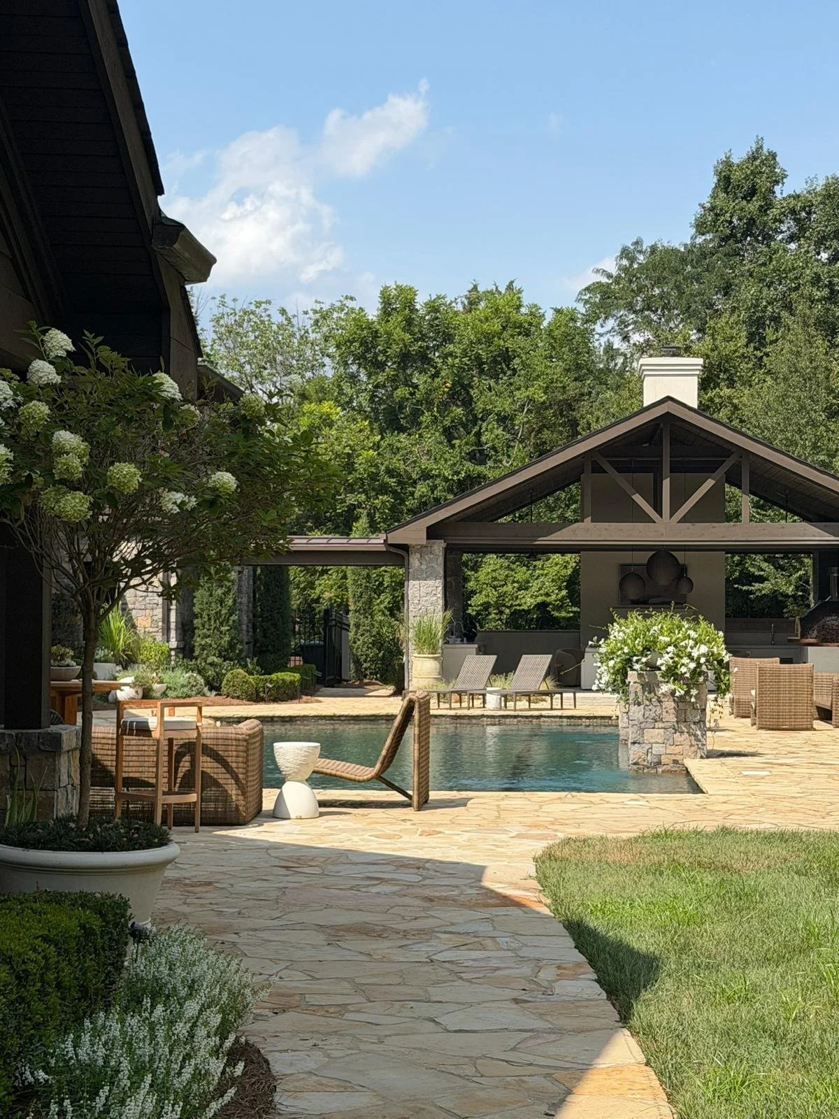 Backyard patio with swimming pool, outdoor lounge chairs, trees, plants, and a covered structure with a barbecue grill. Ultra luxury home for sale in Nashville, TN,  at $12.3M.