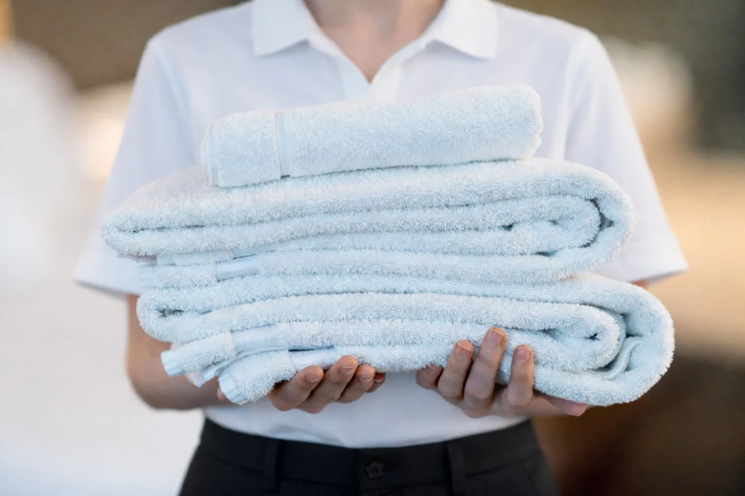 Person in white shirt holding folded white towels.