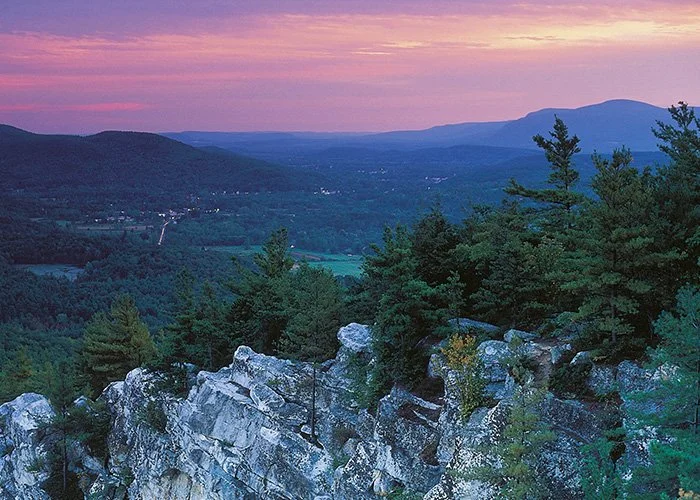 Sunset over a mountainous landscape with forests and rocky ledge in the foreground